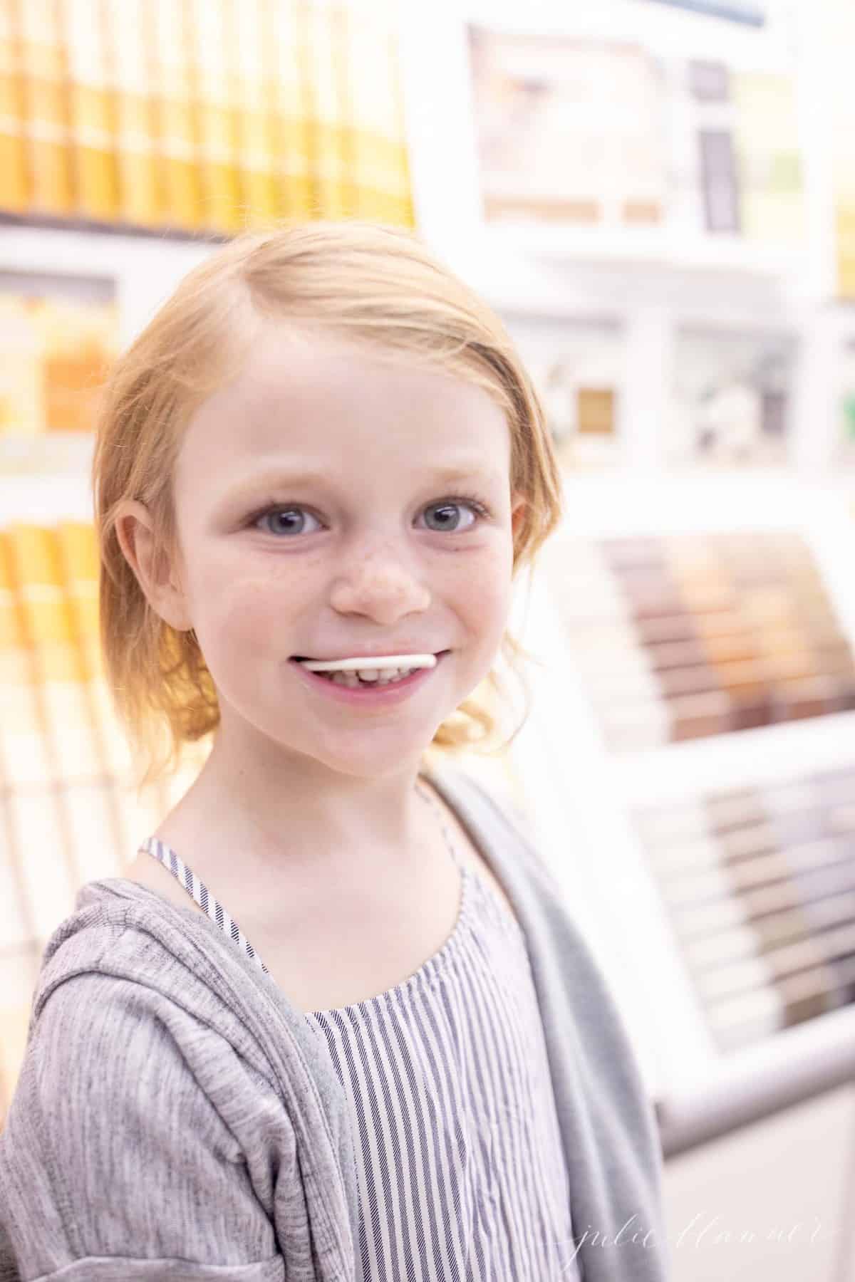 girl with sucker in her mouth in front of paint cards at hardware store