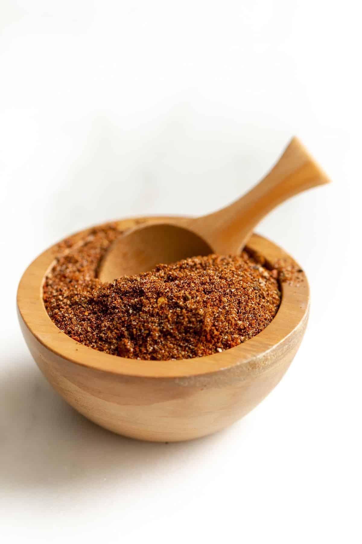 Homemade taco seasoning in a wooden bowl with a wooden spoon. on a white surface.