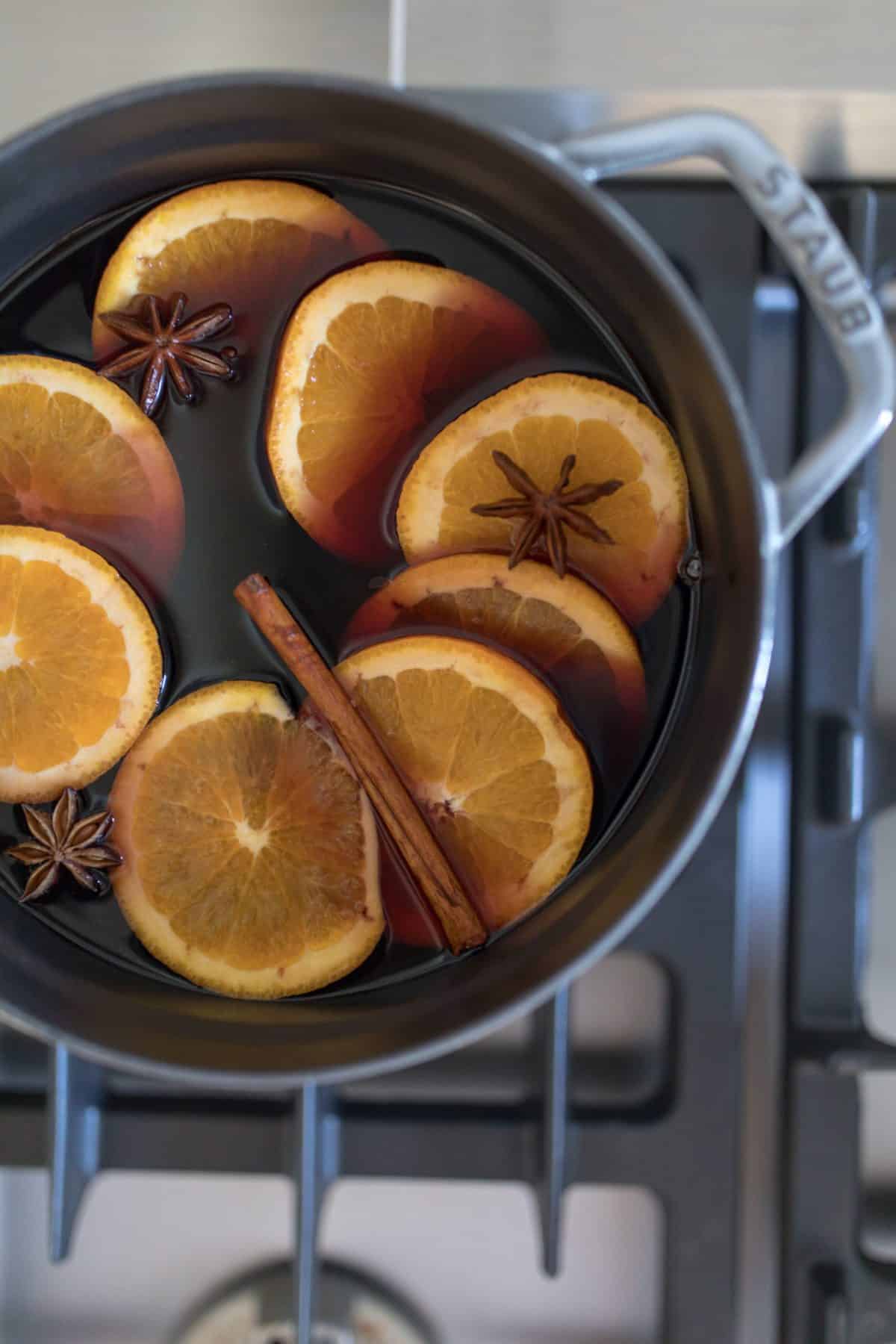 a gray cast iron pot on the stove with mulled wine, orange slices and cinnamon sticks.