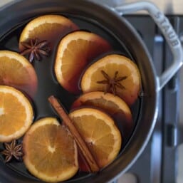 a gray cast iron pot on the stove with mulled wine, orange slices and cinnamon sticks.