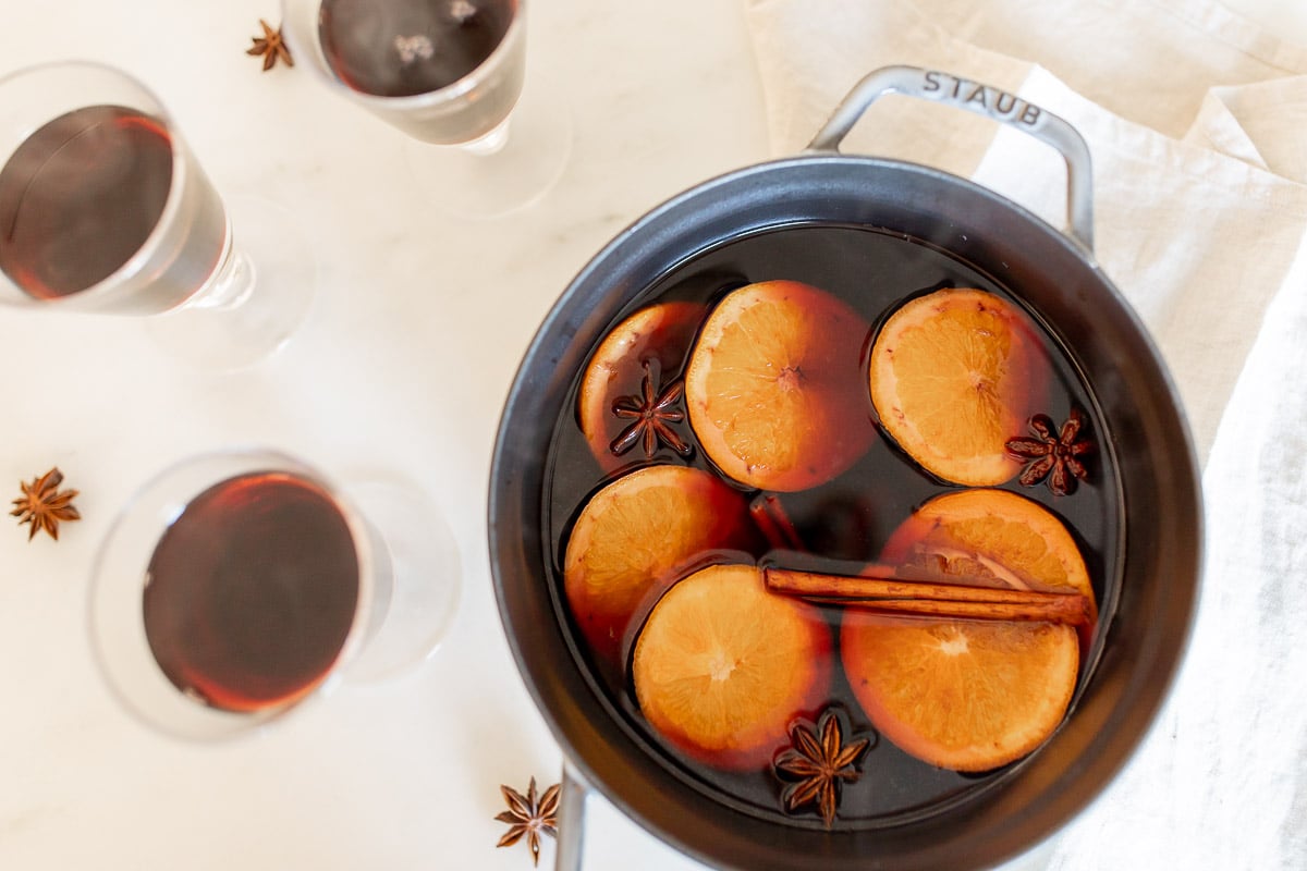 Mulled wine in a cast iron pot, surrounded by glasses of mulled wine. 