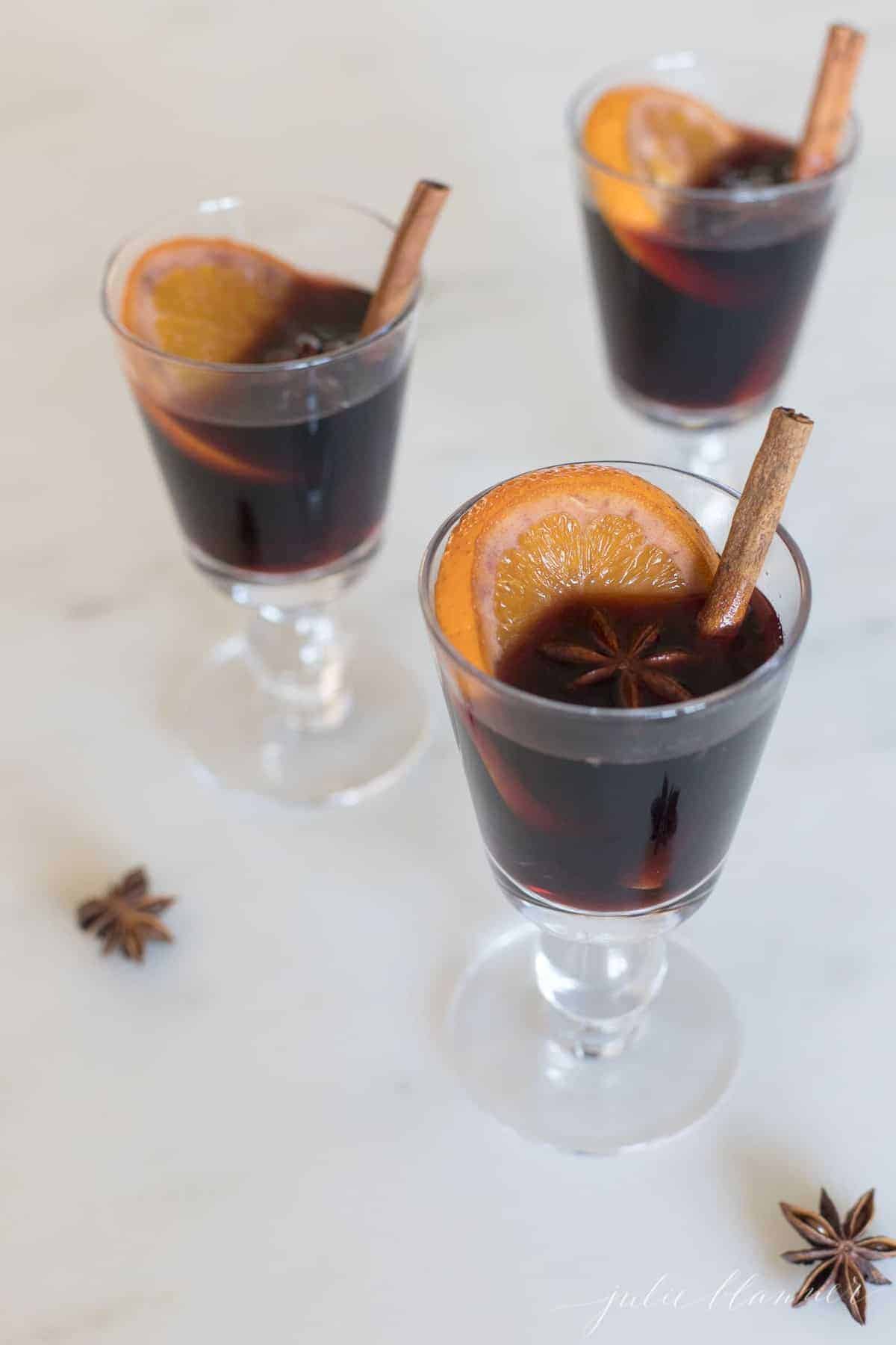 clear glasses full of mulled wine, cinnamon stick and orange slice to the side.