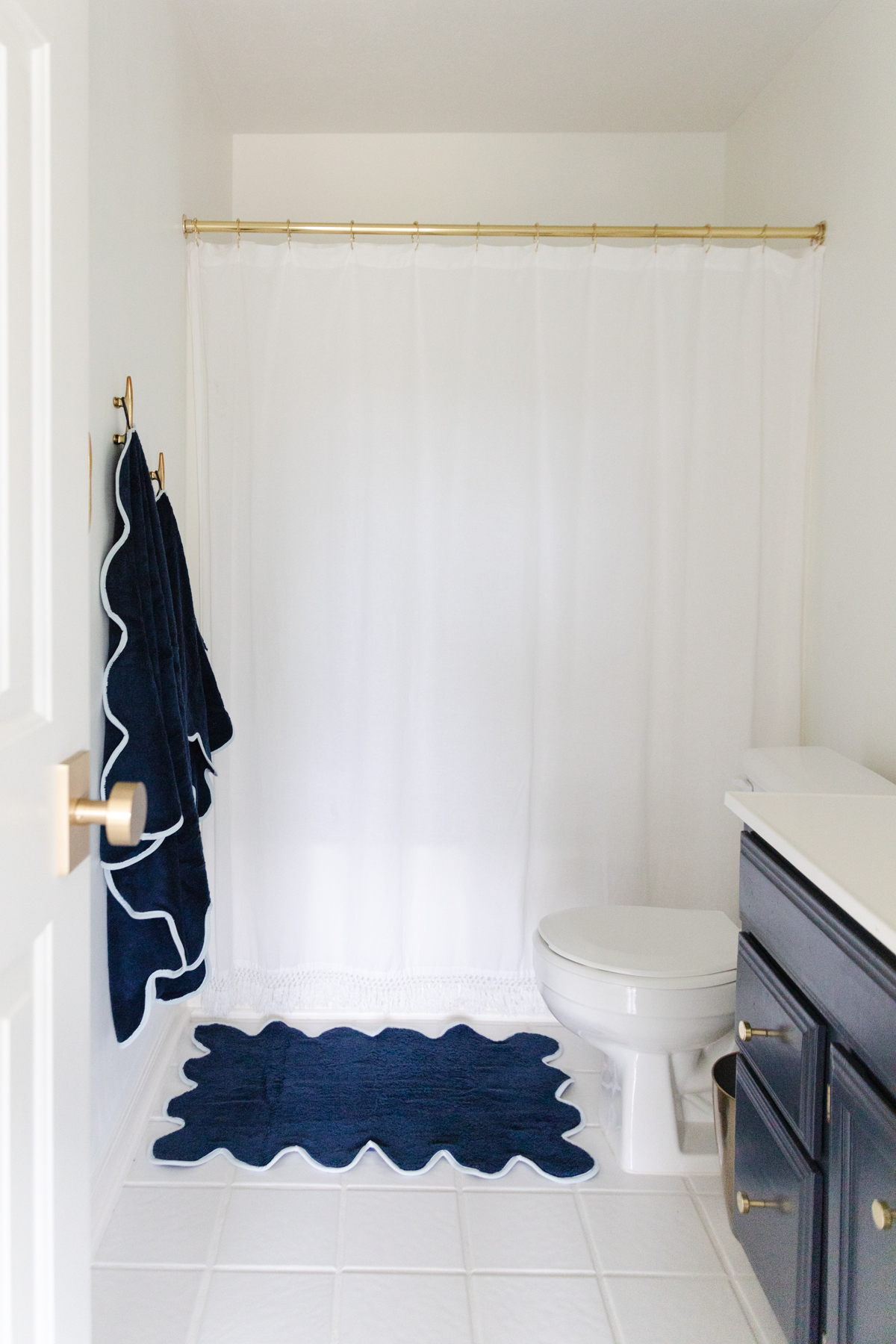 A nautical bathroom with a blue rug and white shower curtain.
