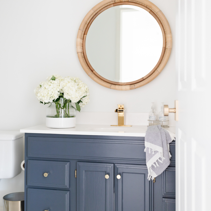 A nautical bathroom with a navy vanity and a rattan round mirror.