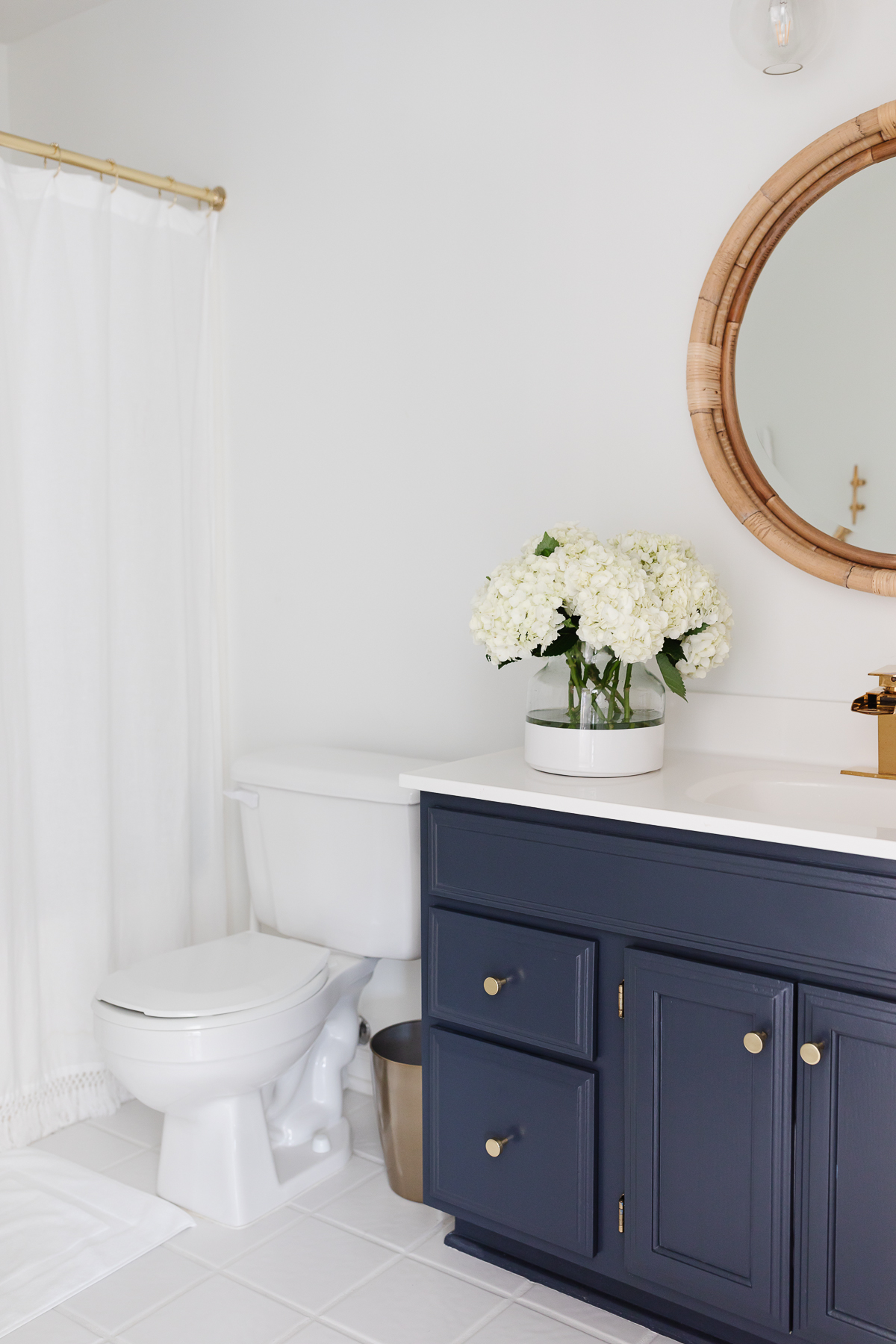 A nautical bathroom with a navy vanity and a rattan round mirror.