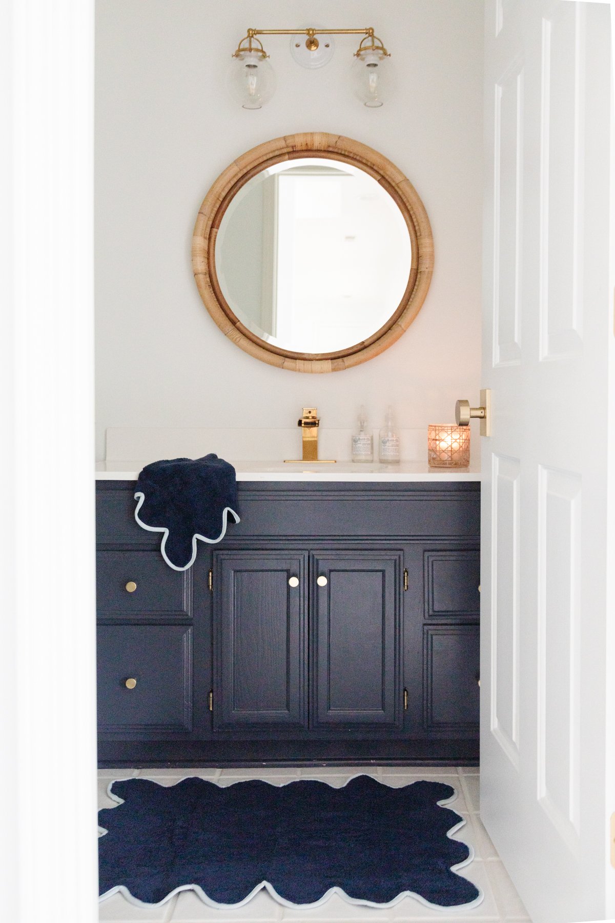 A nautical bathroom decor with navy cabinets and a gold mirror.