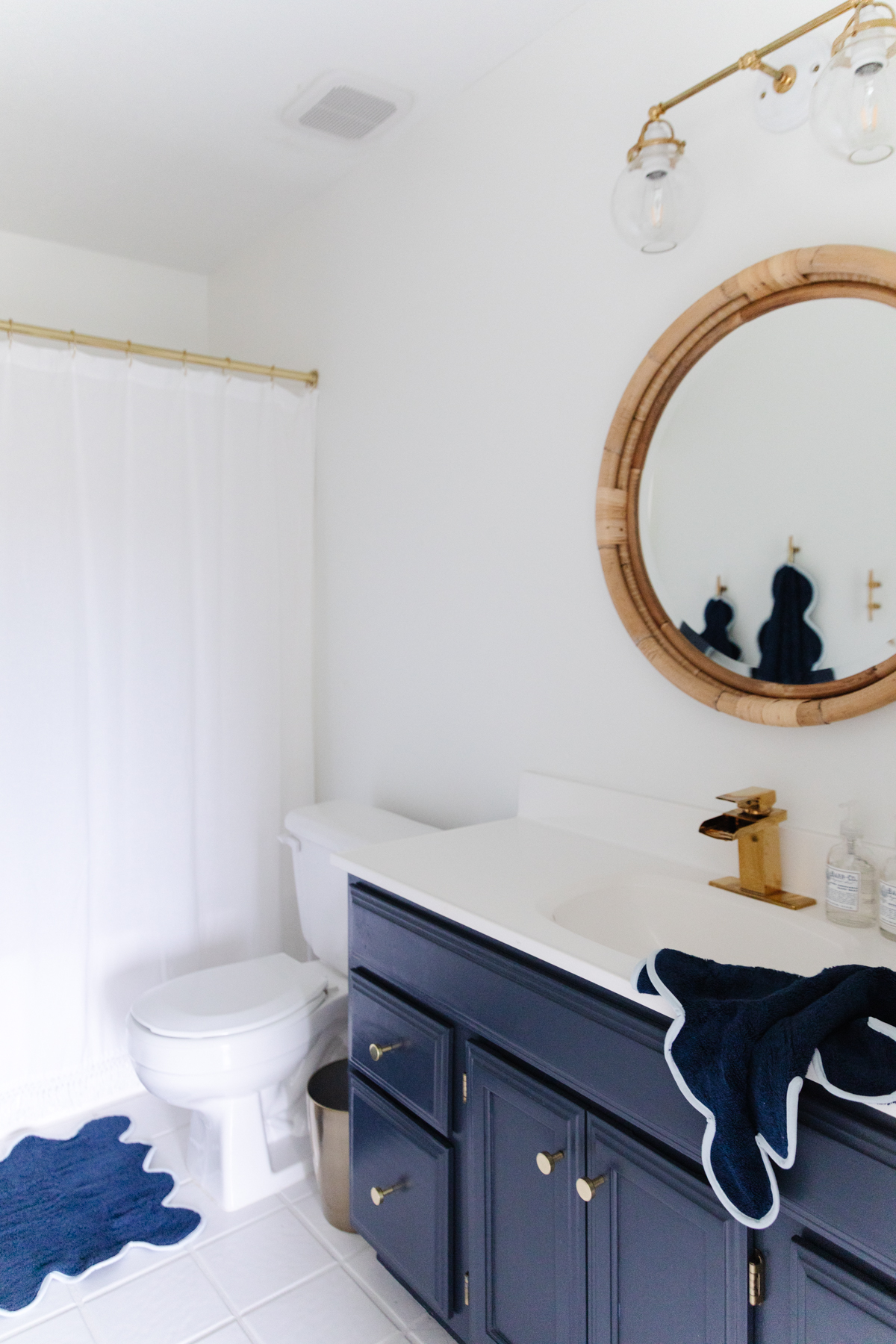 A nautical-themed bathroom with blue cabinets and a round mirror.