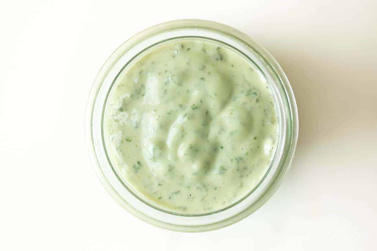 Pesto aioli in a glass jar on a white surface.