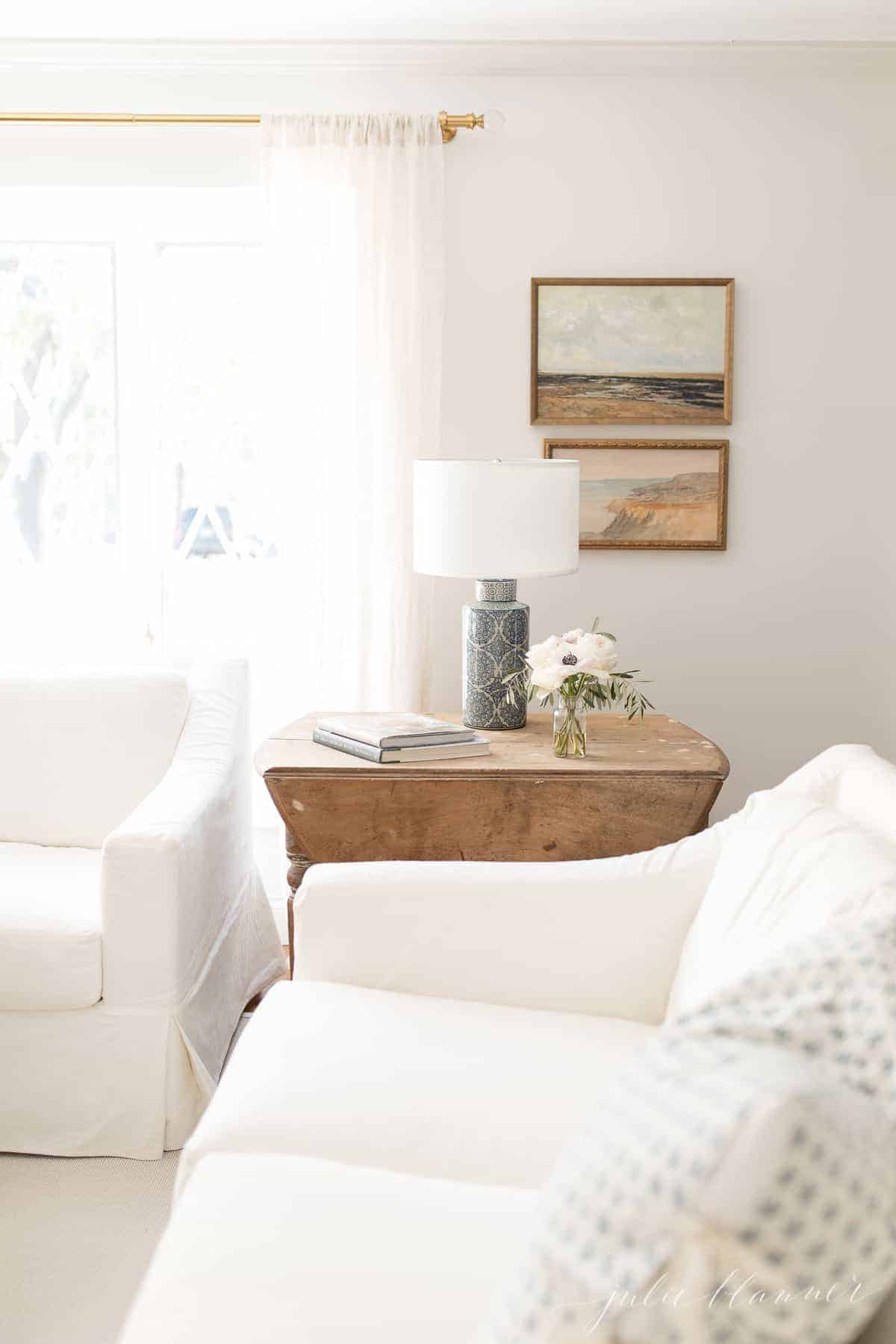 White Pottery Barn slipcovered sofas, antique wooden table with a blue lamp and simple decor in a living room.