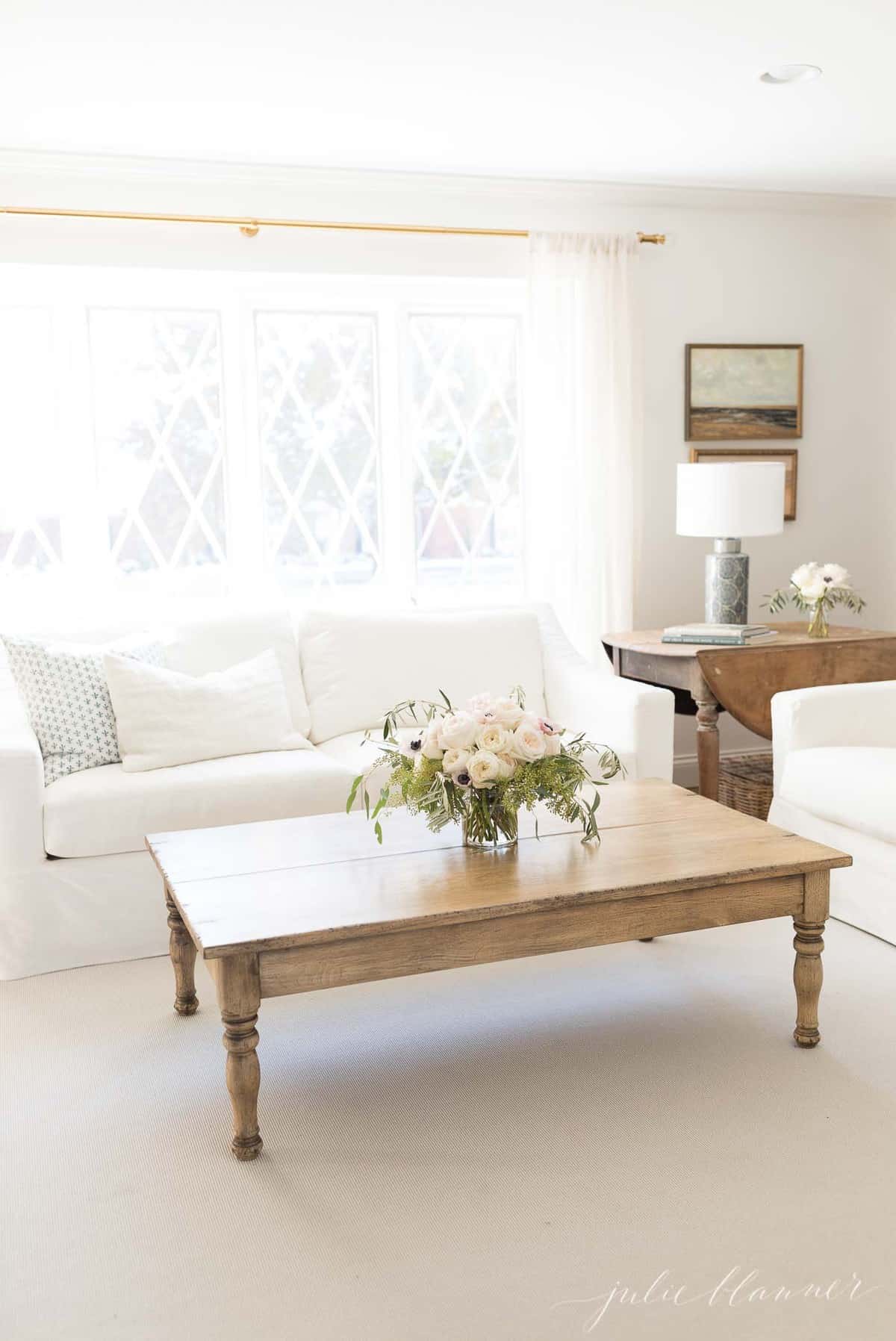 White living room with a white slipcovered sofa in front of a large window, coffee table in front. 