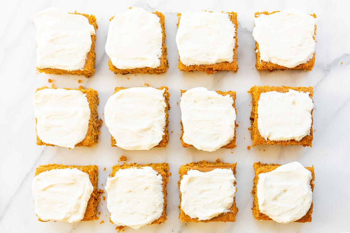 Pumpkin bars with cream cheese frosting on a white countertop.
