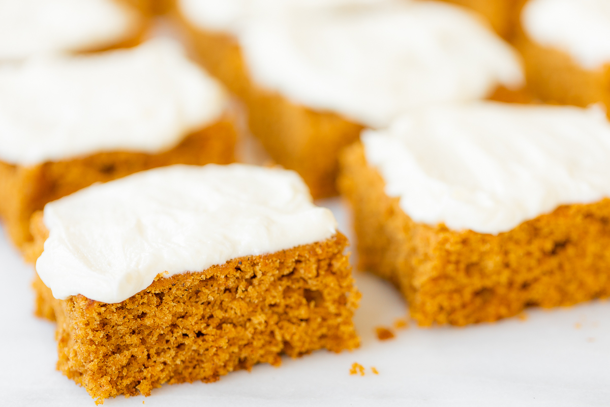 Pumpkin bars with cream cheese frosting on a marble surface.