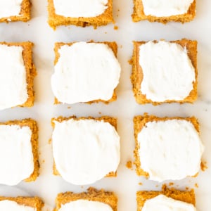 Pumpkin bars with cream cheese frosting on a marble surface.