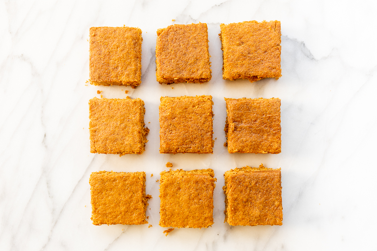 Squares of a pumpkin bar recipe laid out on a marble countertop.
