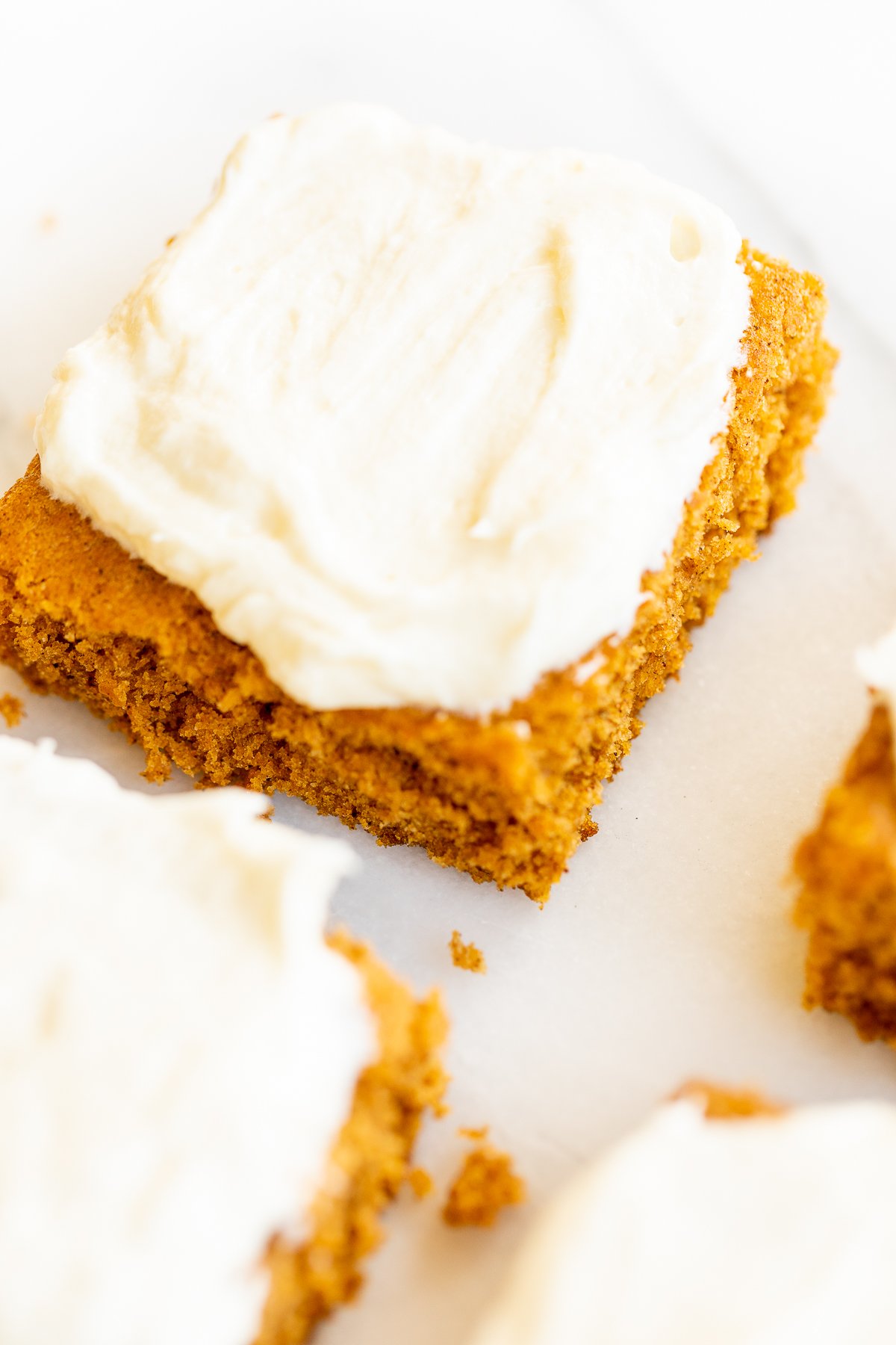 Pumpkin bars with cream cheese frosting on a marble surface.