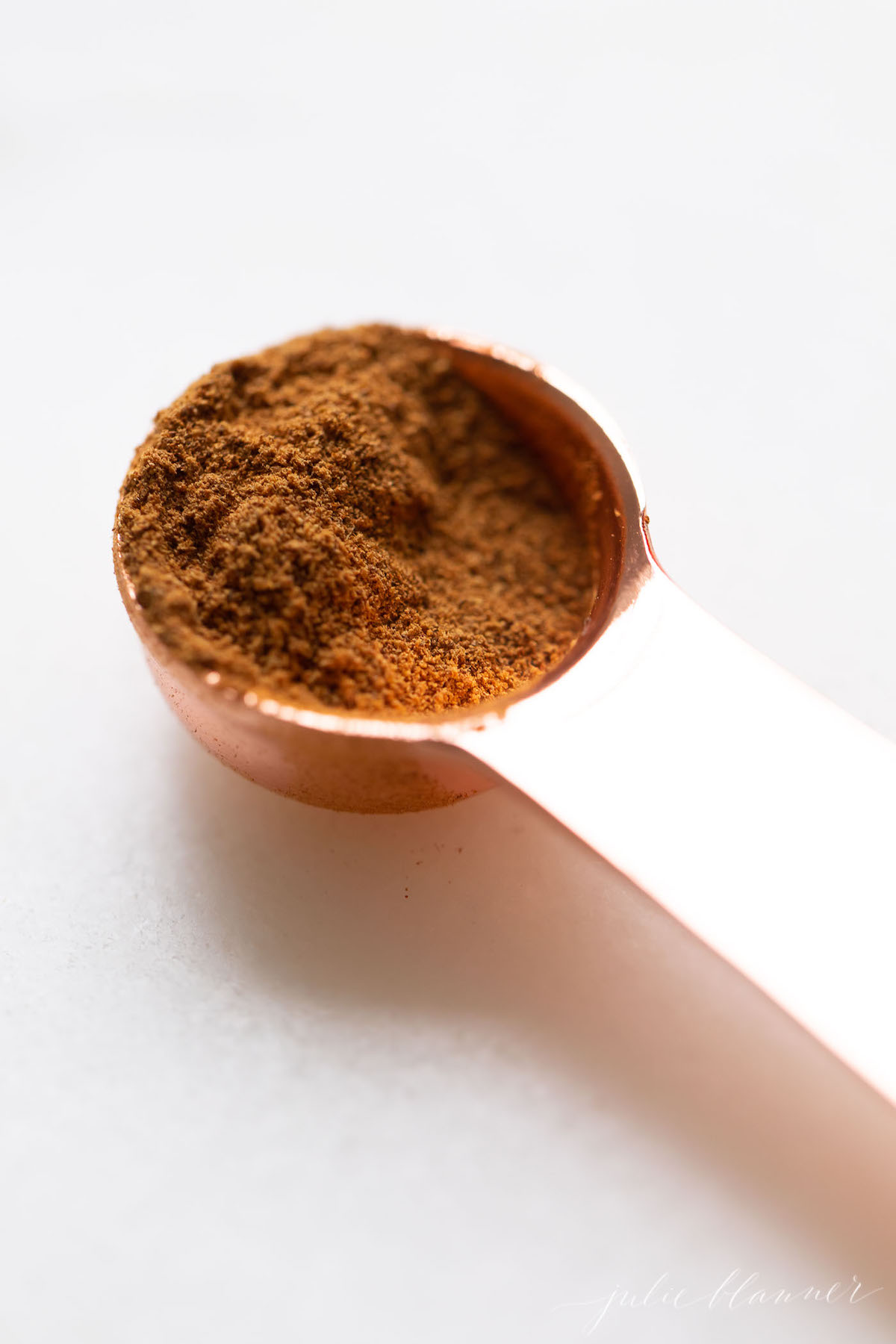 A copper teaspoon full of homemade pumpkin pie spice on a white countertop.
