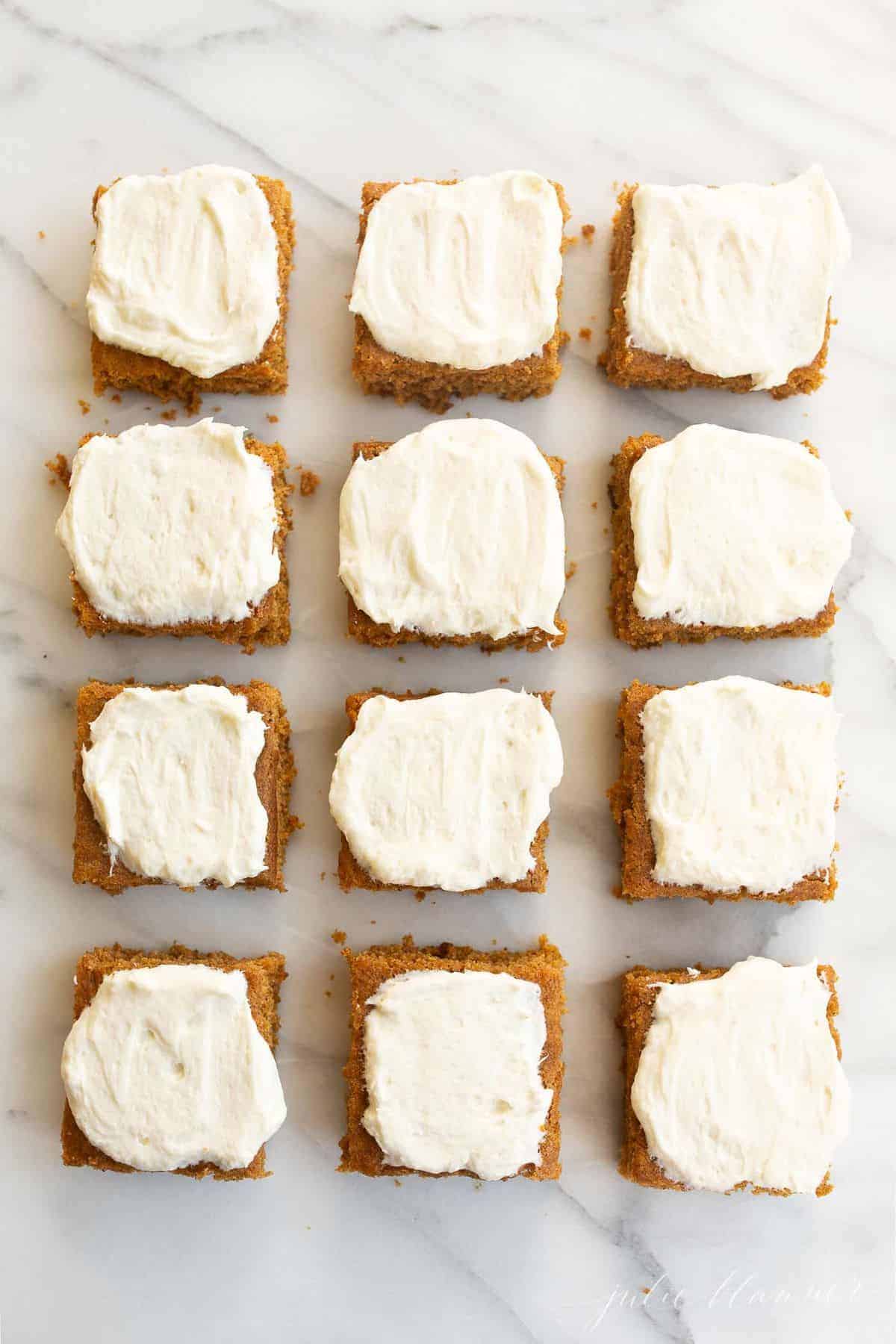 White surface with 12 cut pumpkin squares covered in frosting. 