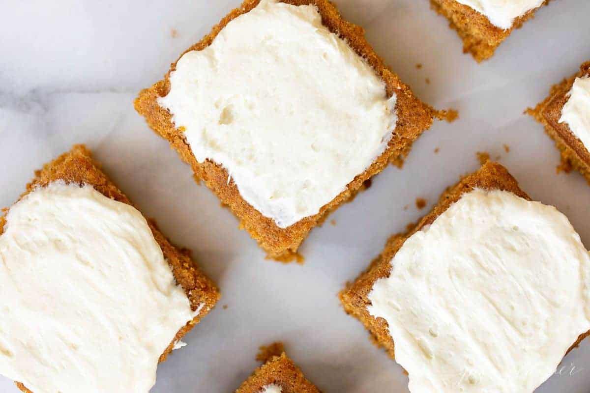 White marble surface with a close up of pumpkin bars cut and covered in cream cheese frosting.