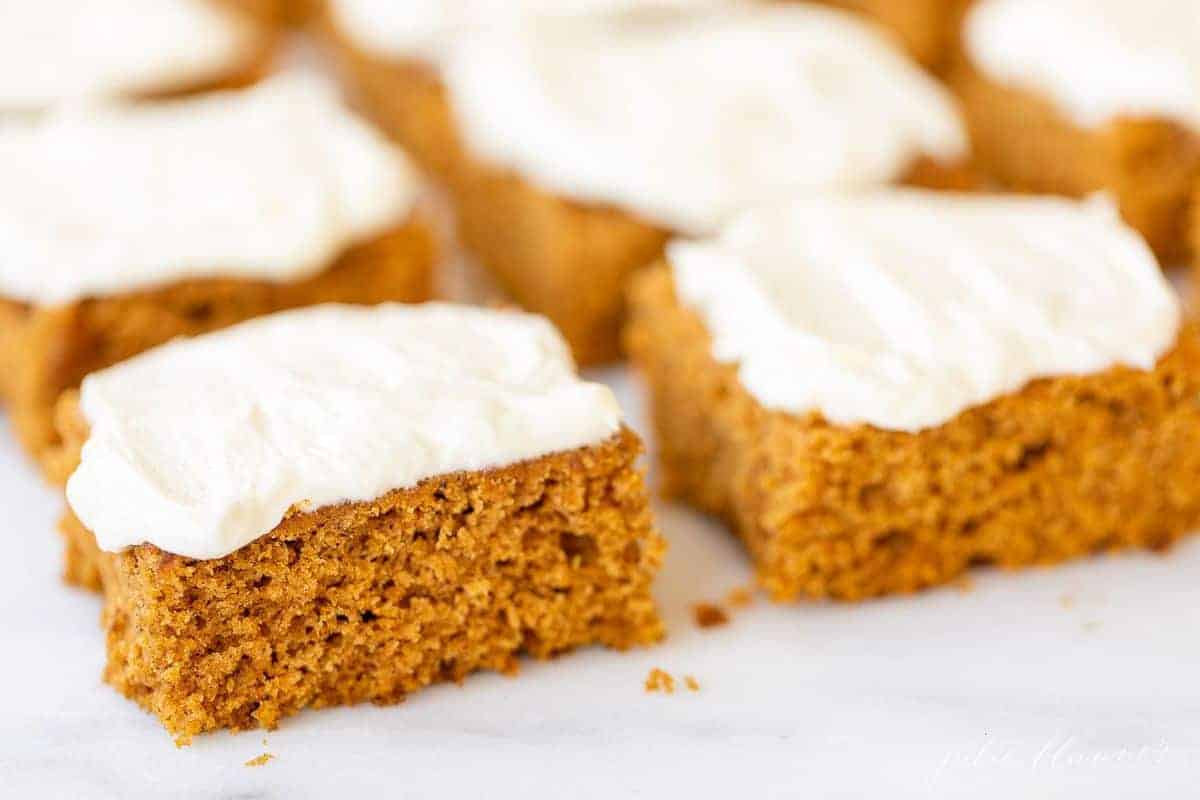 White marble surface with a close up of pumpkin bars cut and covered in cream cheese frosting.
