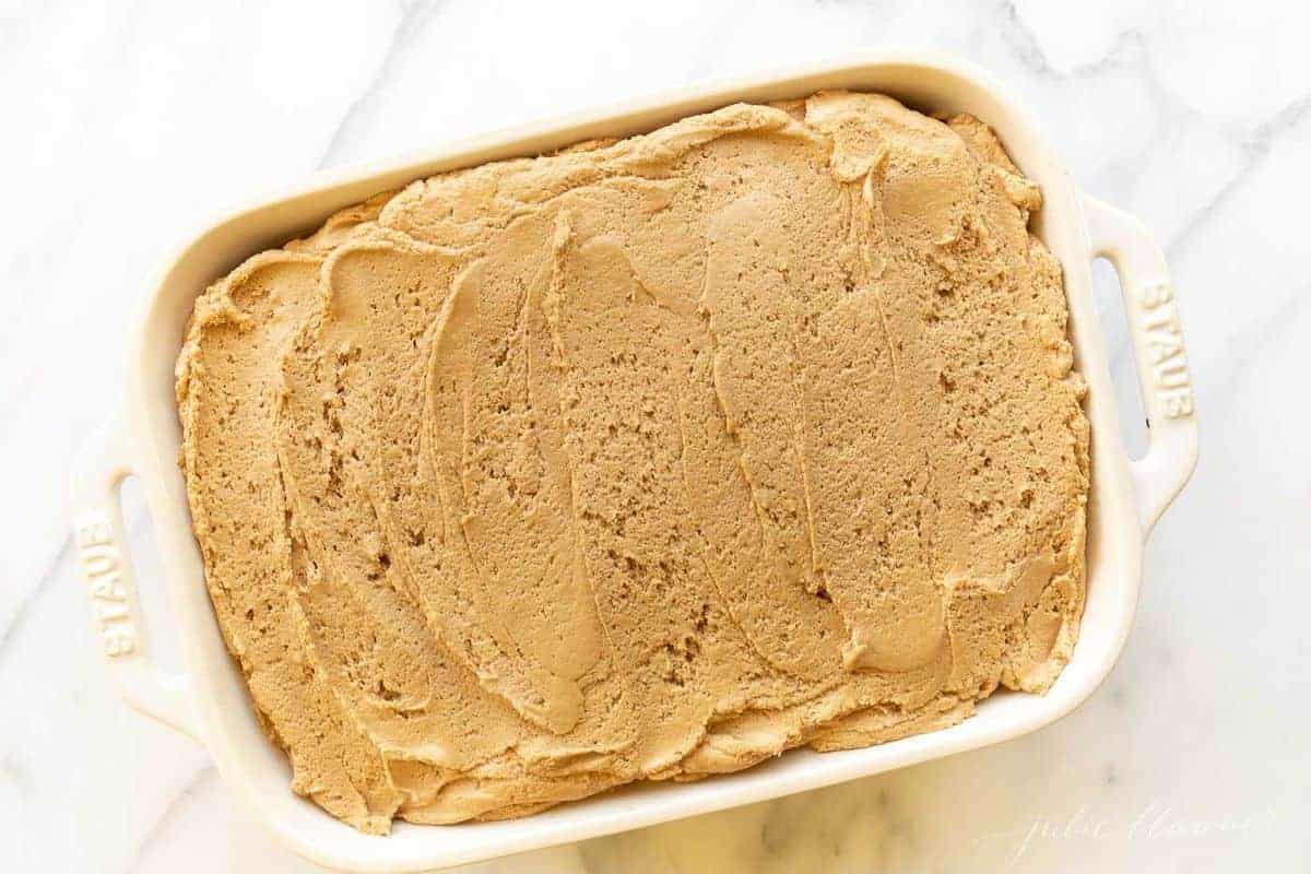 A white baking dish with a cookie butter cake and frosting slathered on top.