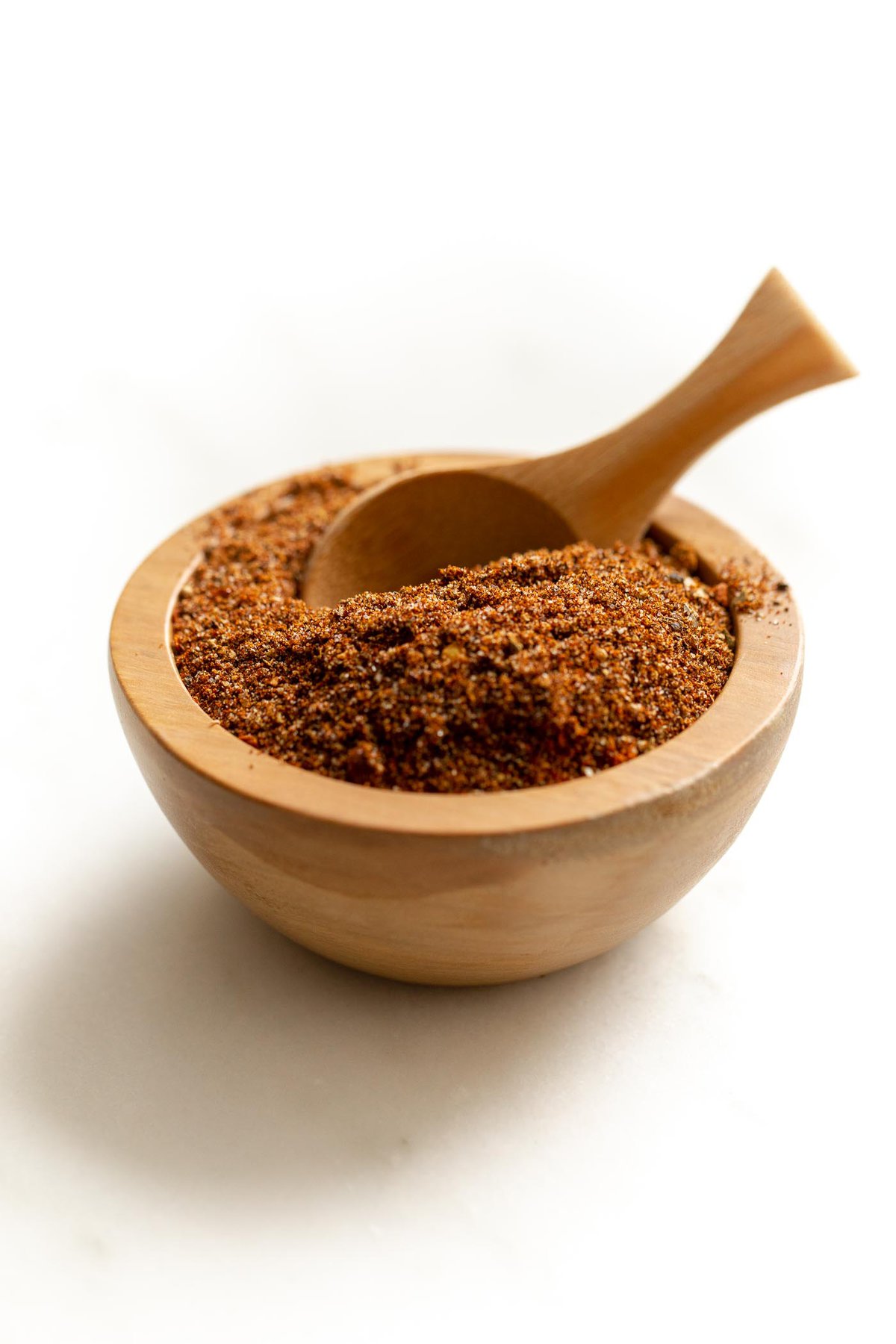 A small wooden bowl full of homemade taco seasoning, with a wooden teaspoon inside.