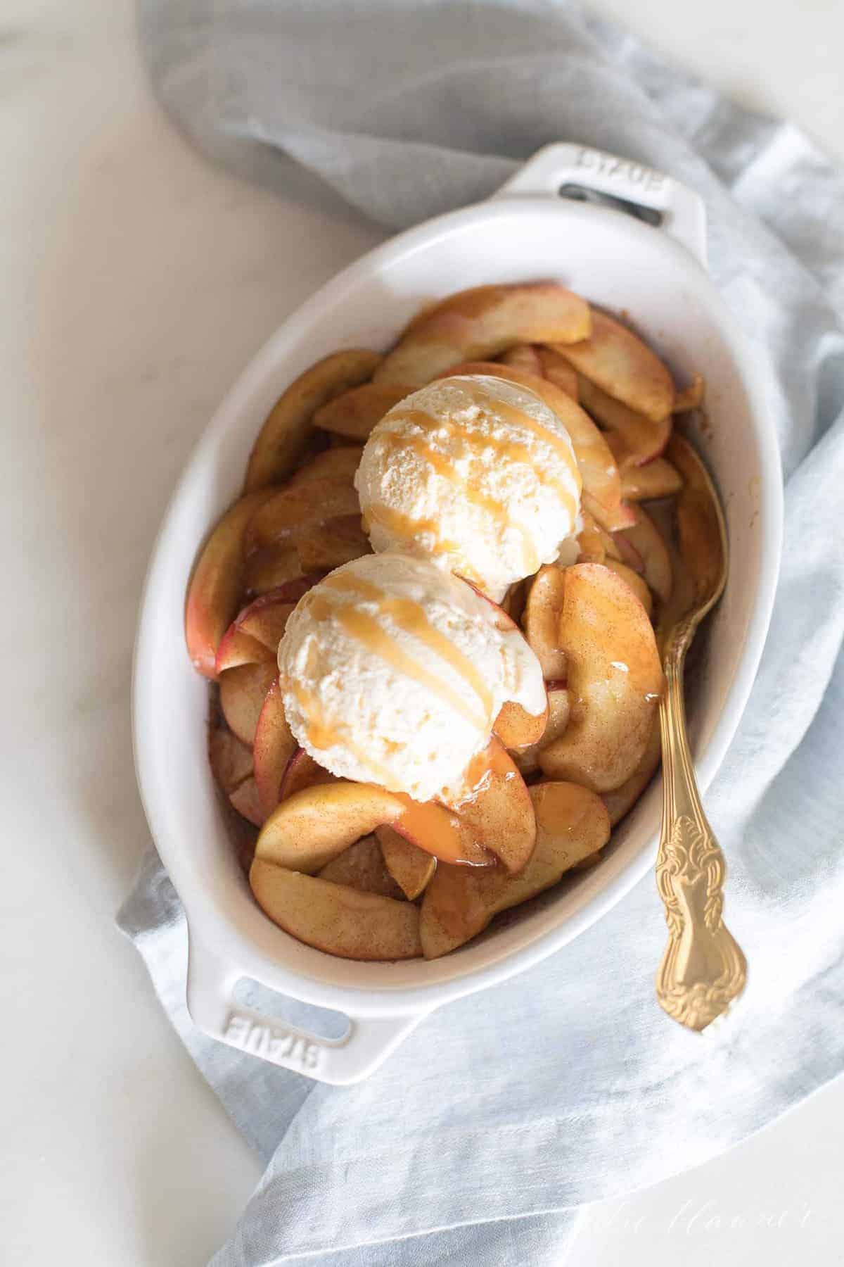 White surface, towel to the side, with a big white baking dish full of baked apples topped with ice cream.