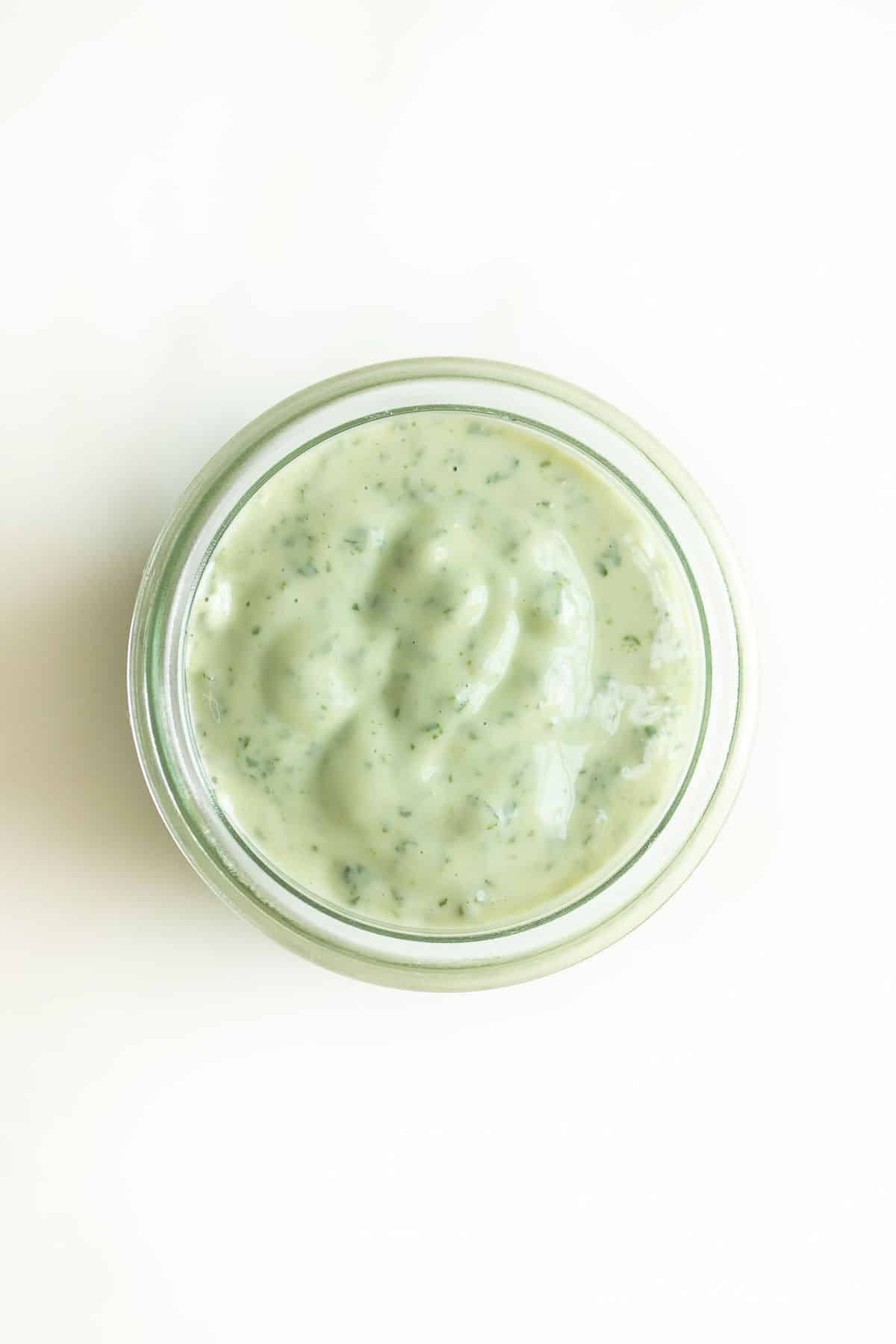 Pesto aioli in a glass jar on a white surface.