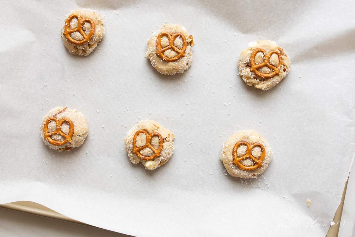 Toffee Chocolate chip cookies with pretzels on top, on a lined baking sheet ready to go into the oven.