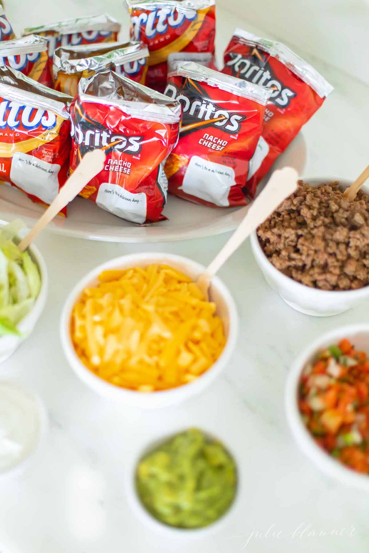 A marble counter set up with chip bags and toppings for a walking taco recipe.