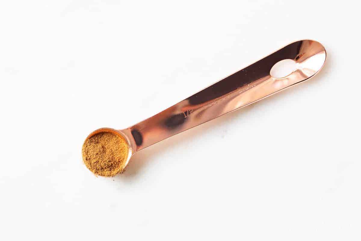 White surface, copper teaspoon filled with pumpkin pie spice mix.