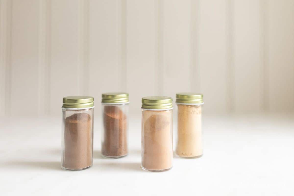 White background with four glass jars of spices, gold lids.