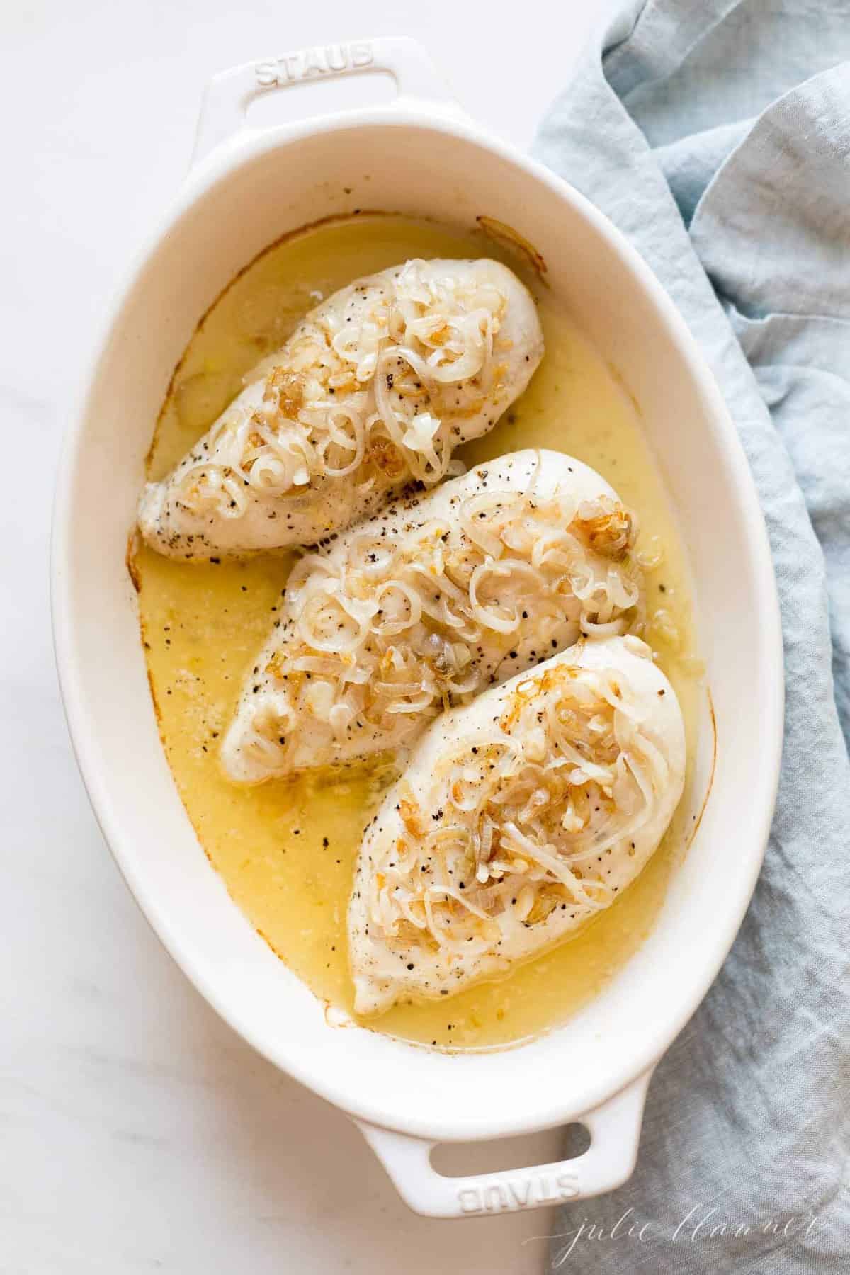 White baking dish featuring 3 baked chicken breasts in sauce.