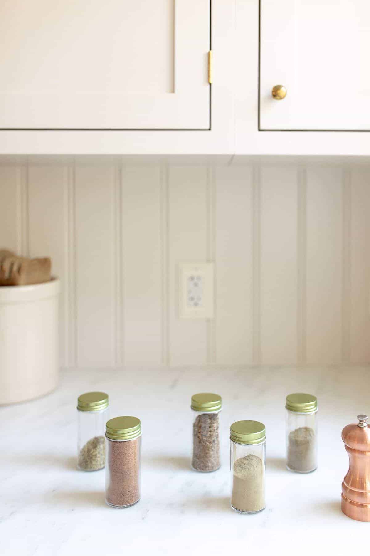 White kitchen with jars of spices in a row for poultry seasoning mix.