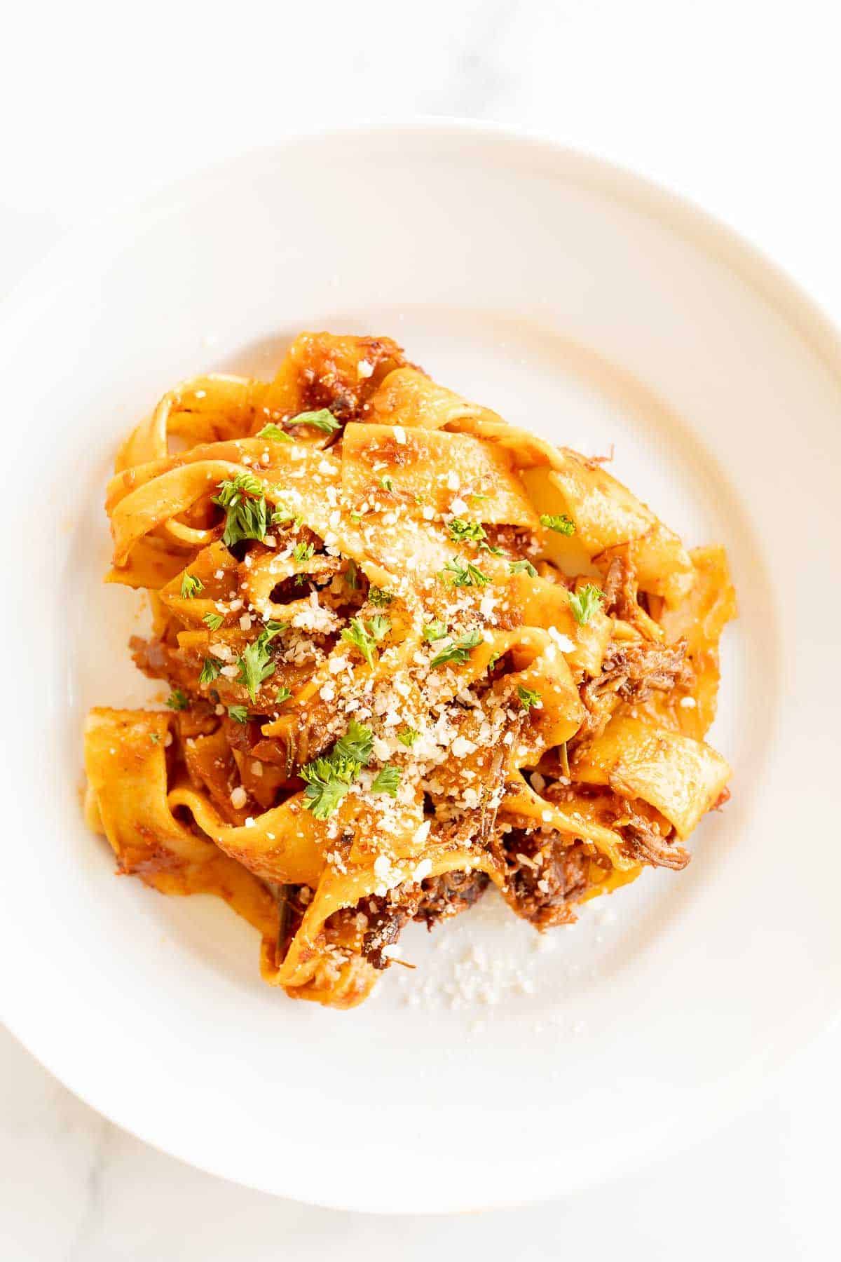 A small white plate with pappardelle pasta, emulsified with a red sauce.