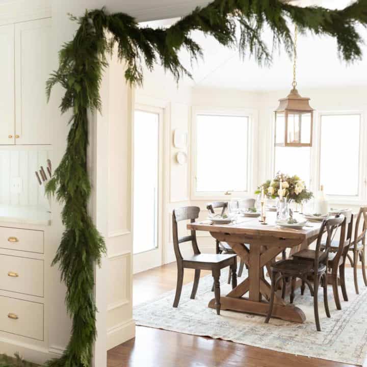 traditional kitchen draped in garland peeking into breakfast nook with blue christmas flower arrangement