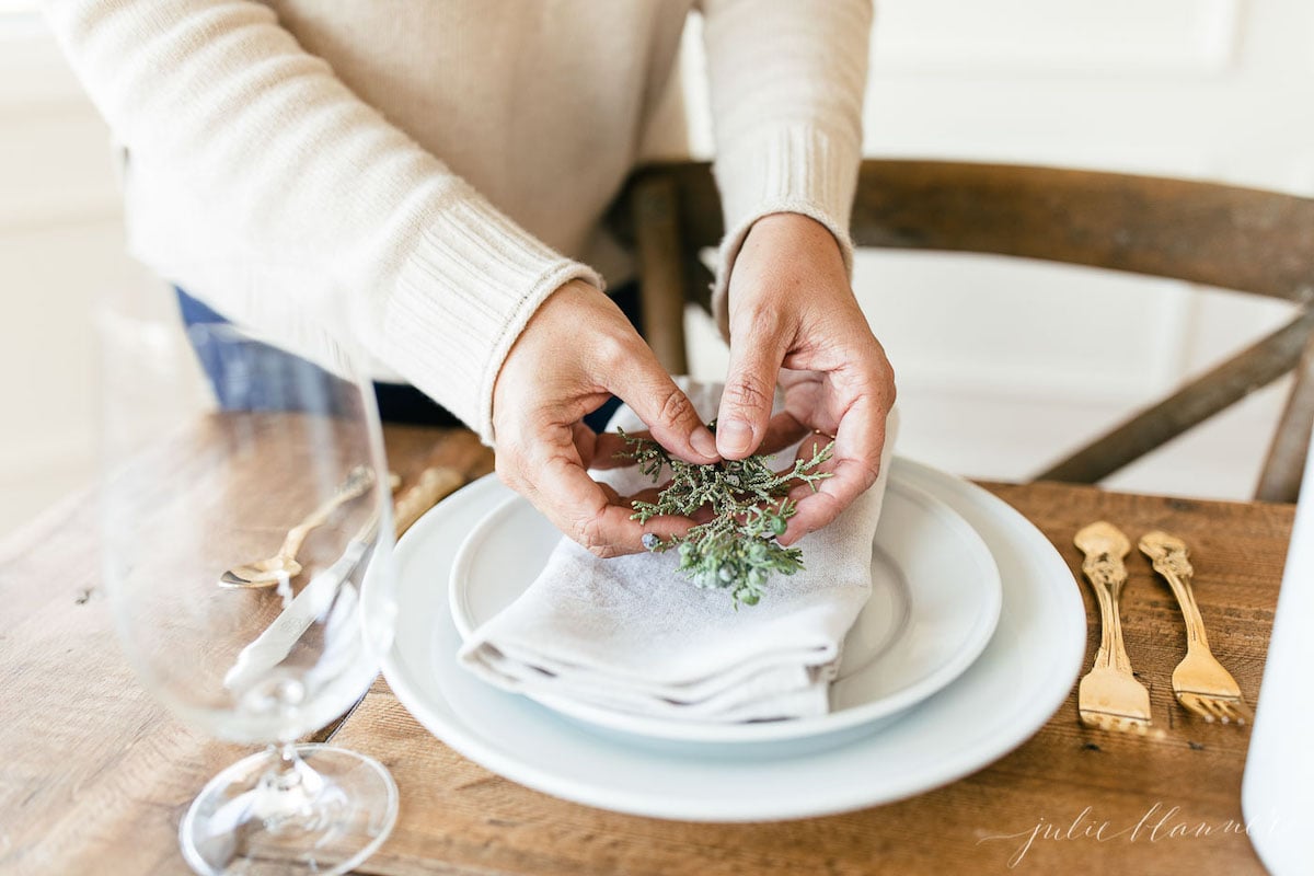 A woman placing sprigs of sage on a table setting.