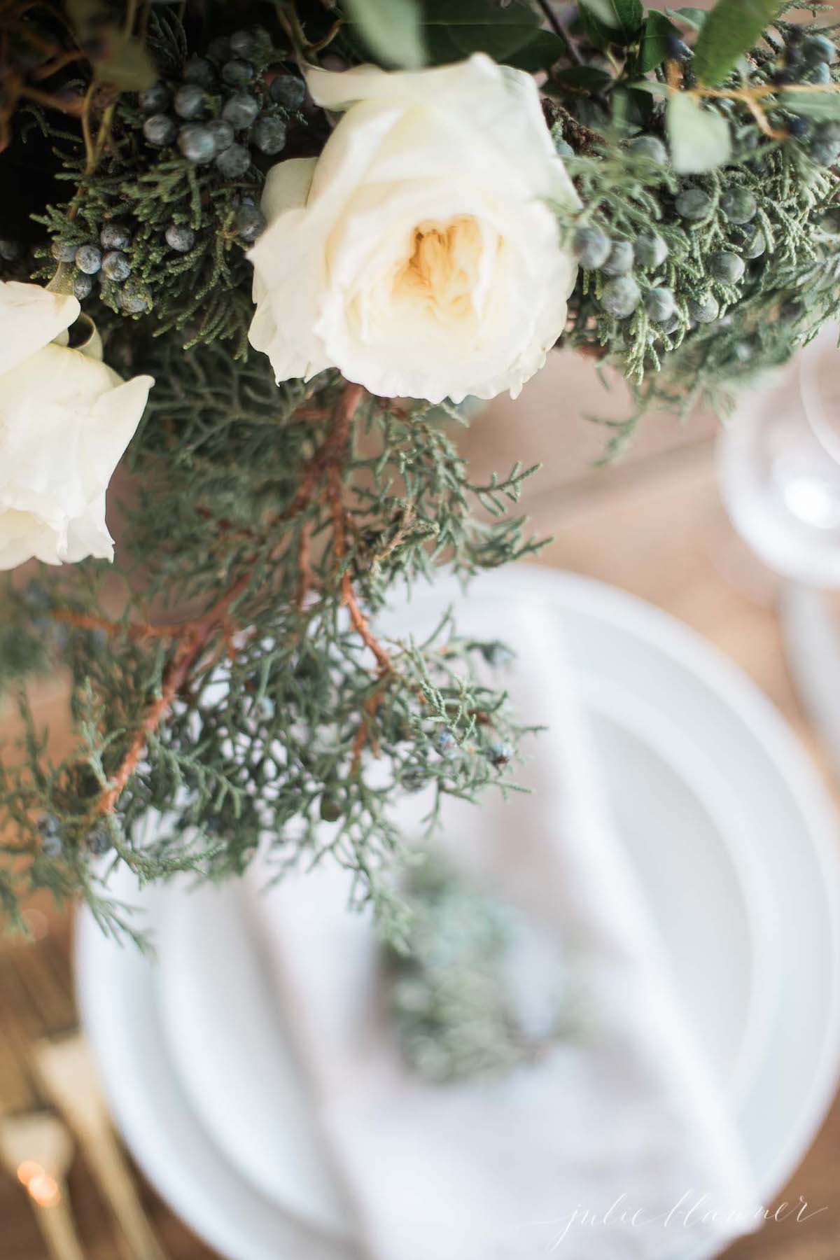 A table setting with white roses and greenery.