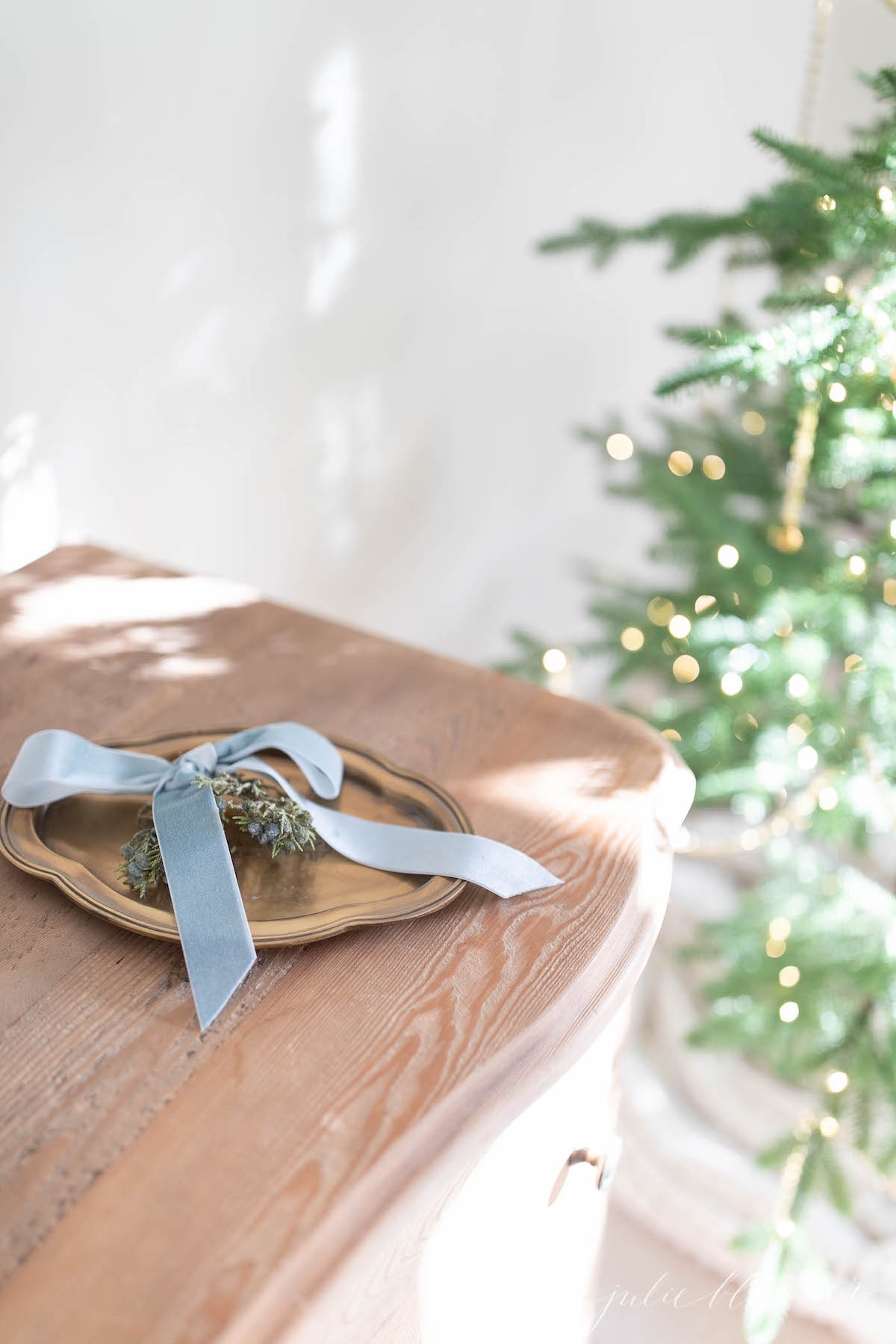 A blue ribbon adorns a wooden table next to a Christmas tree, combining blue and holiday decor elements.