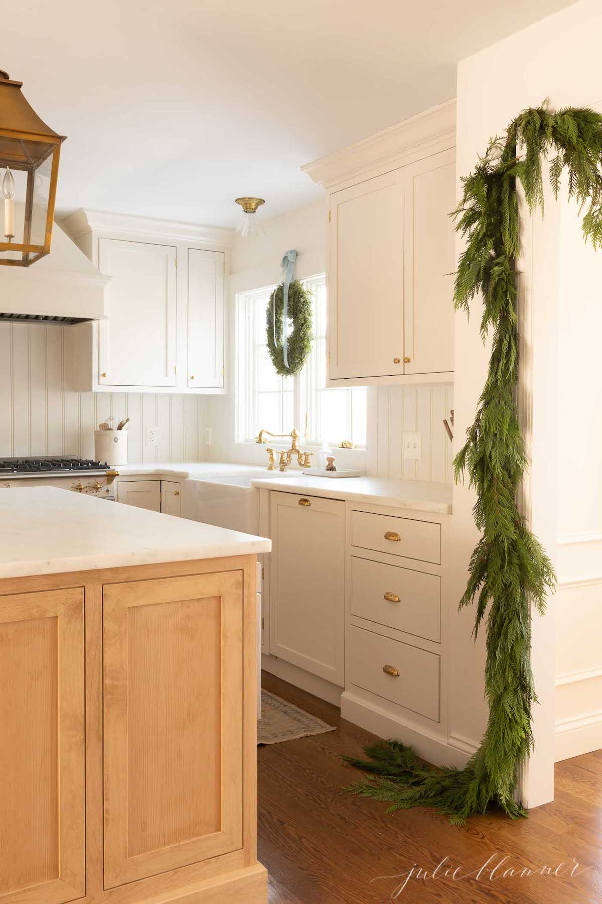 A kitchen adorned with a festive green garland and featuring sleek white cabinets.
