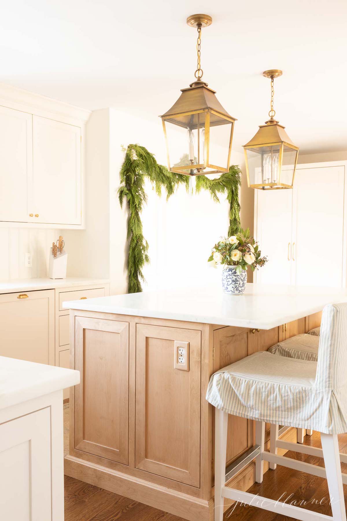 A white kitchen with a white island adorned with greenery for a touch of holiday cheer.