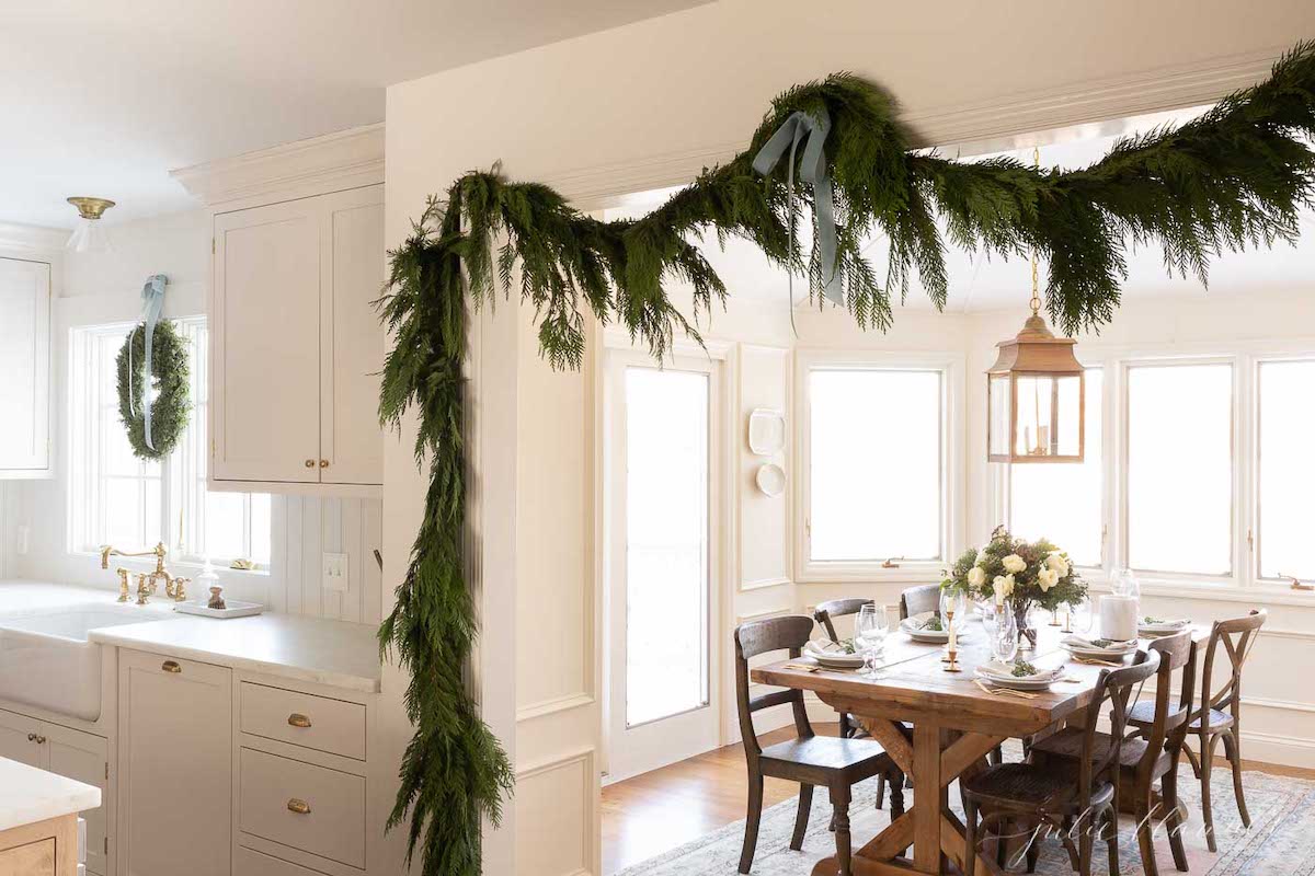A dining room in a holiday home with a garland and blue Christmas decorations hanging over the dining table.