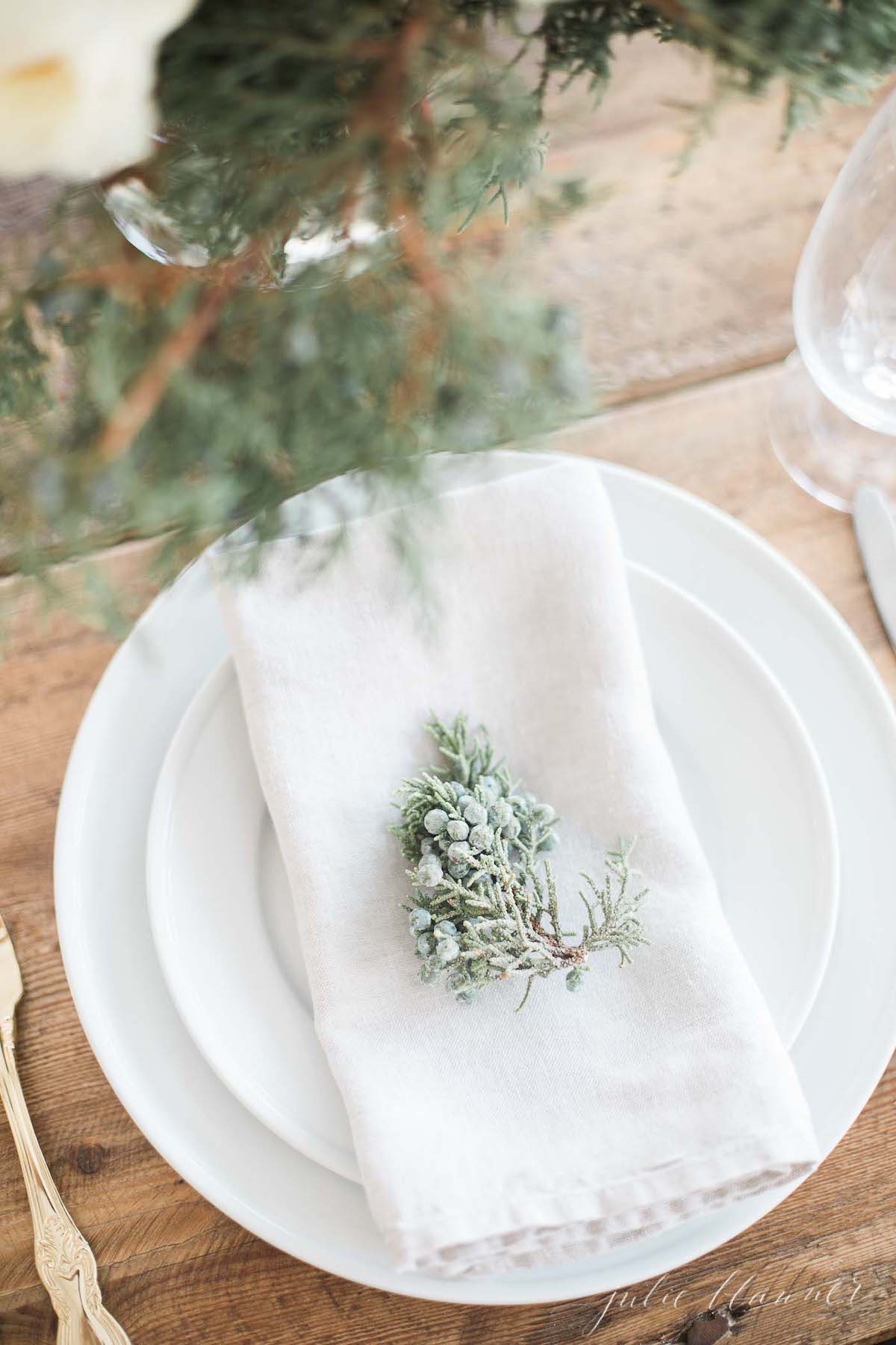 A table setting with a white napkin and greenery adorned with blue Christmas decorations.