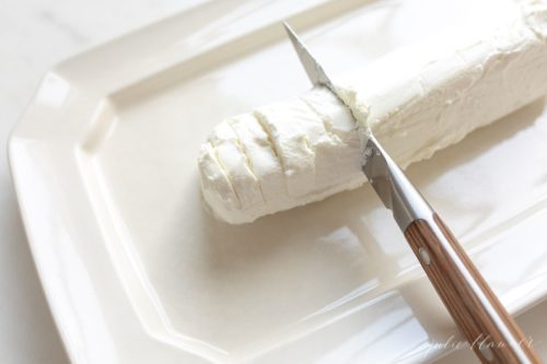 White platter with a log of chevre cheese, knife slices into it.