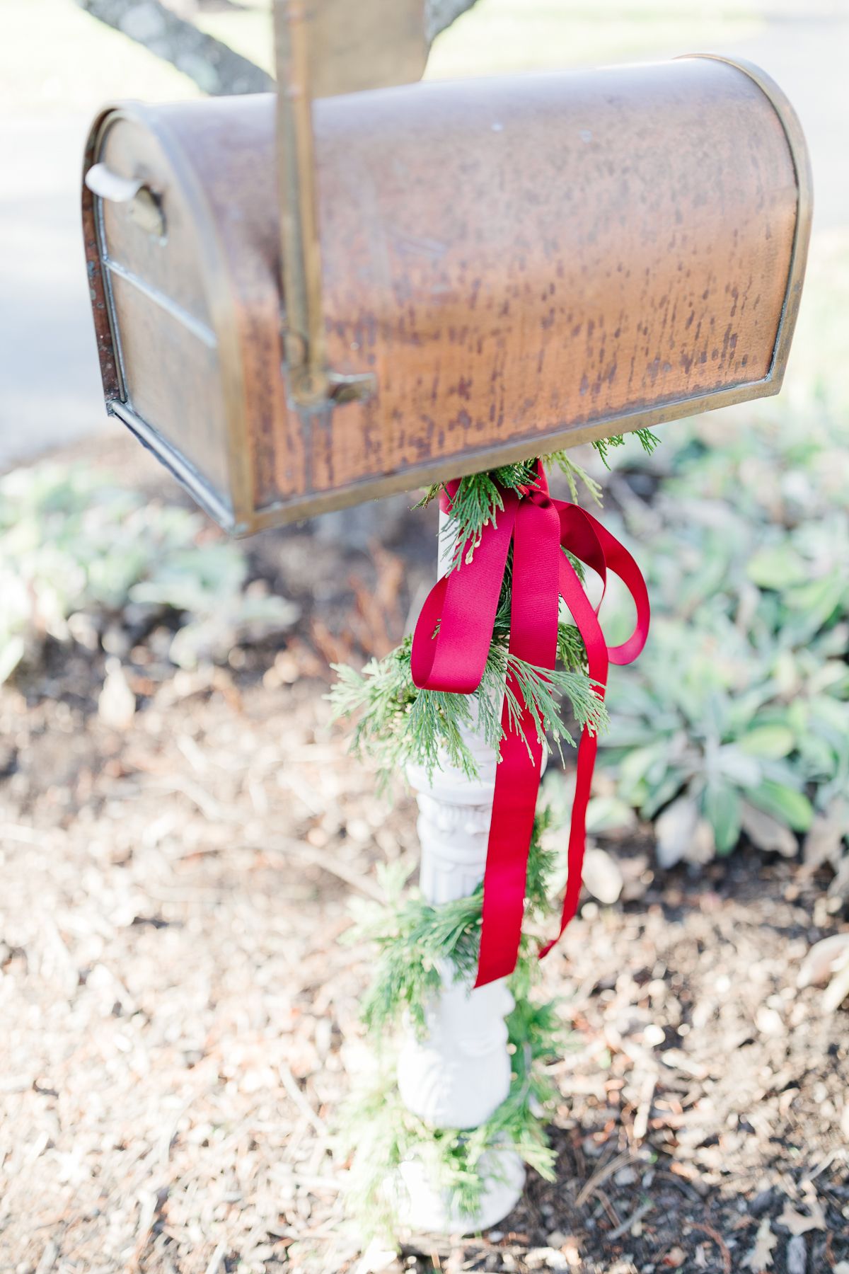 A copper mailbox with Christmas mailbox decorations of a cedar garland and a red bow.