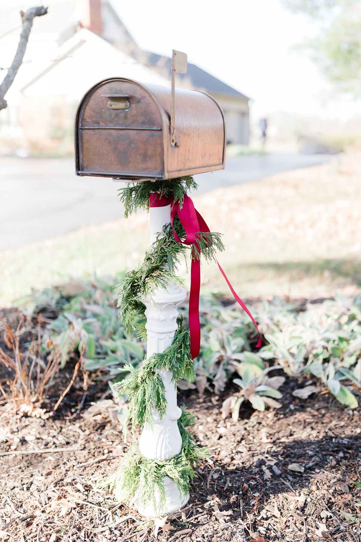 A copper mailbox with Christmas mailbox decorations of a cedar garland and a red bow.