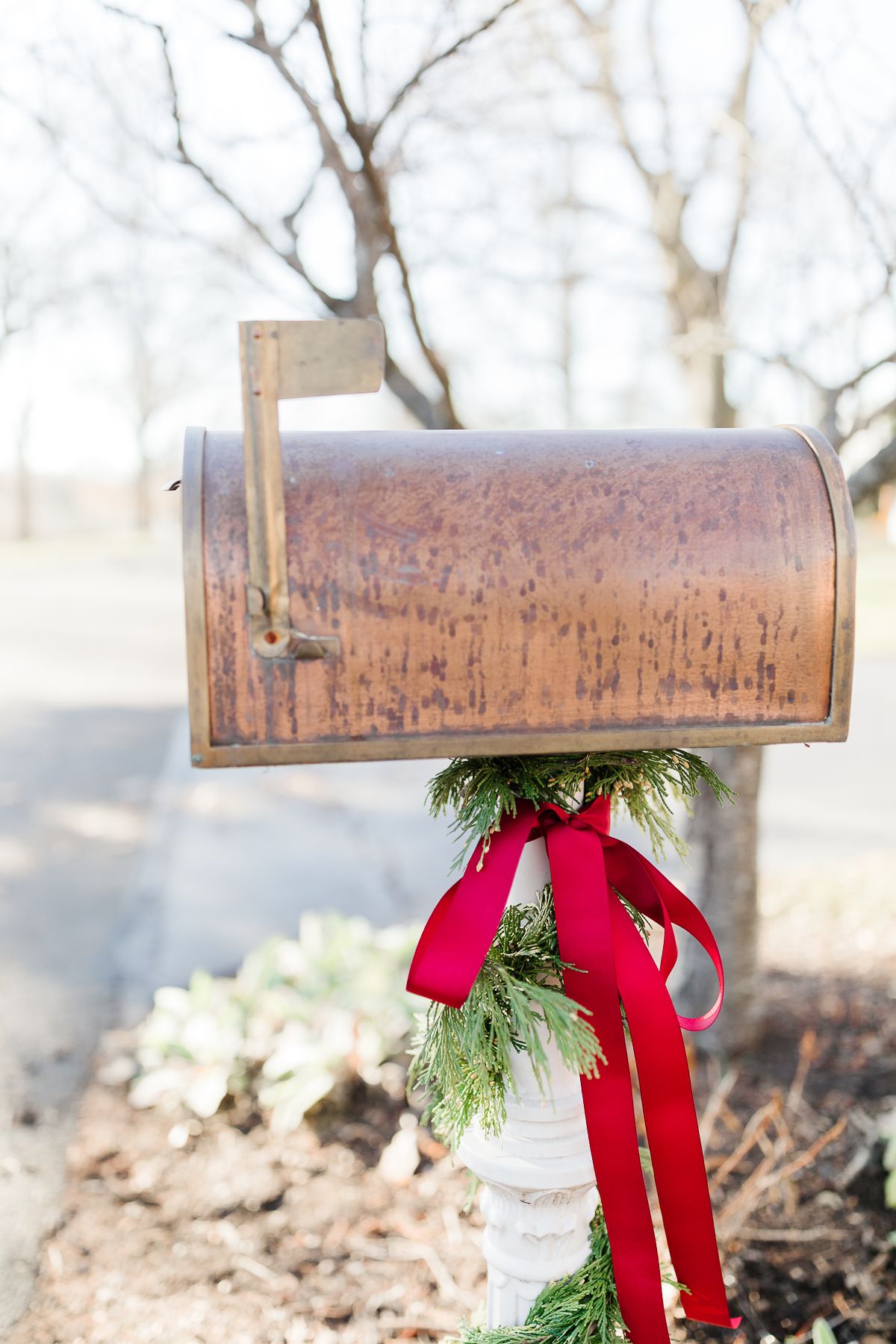 A copper mailbox with Christmas mailbox decorations of a cedar garland and a red bow.