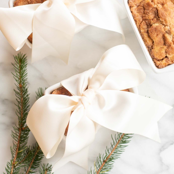 Small loaves of cinnamon bread, tied with ivory ribbon on a marble countertop for a Christmas gift.