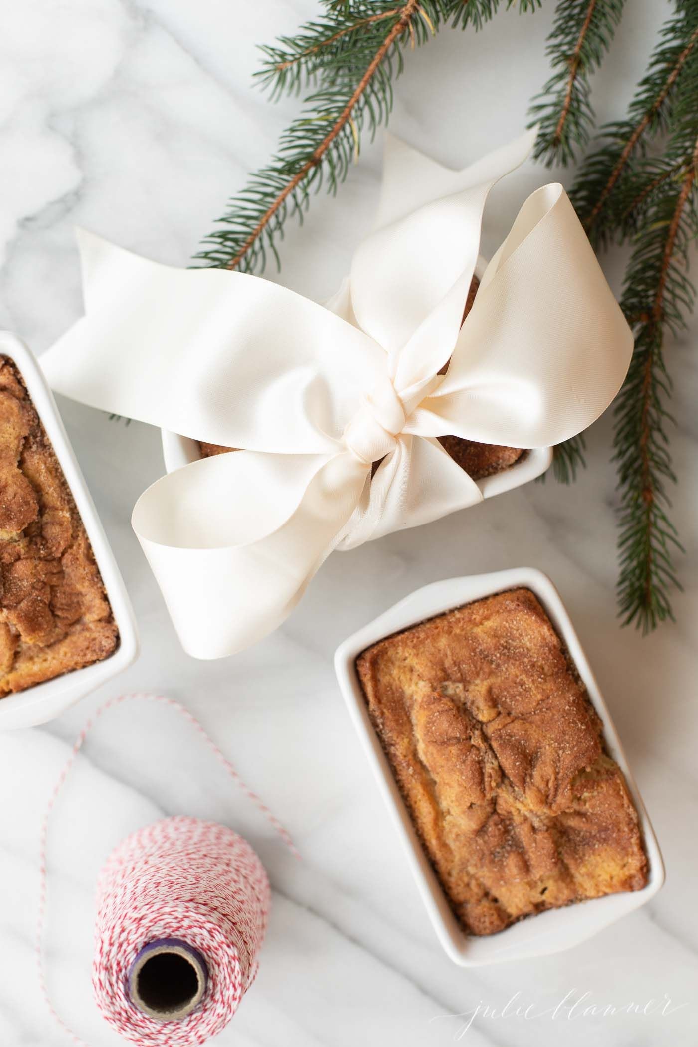Small loaves of cinnamon bread, tied with ivory ribbon on a marble countertop for a Christmas gift.