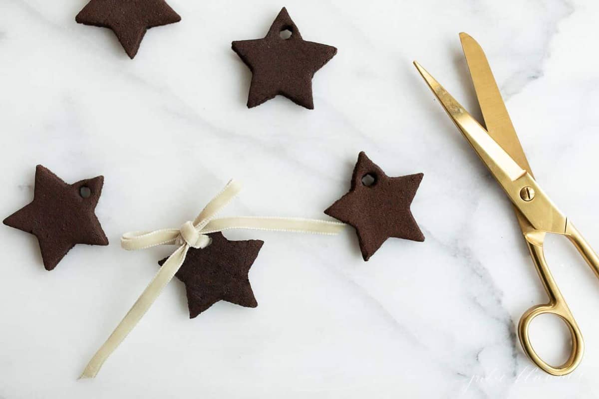 Cinnamon ornaments in the shape of stars on a marble surface, gold scissors to the side