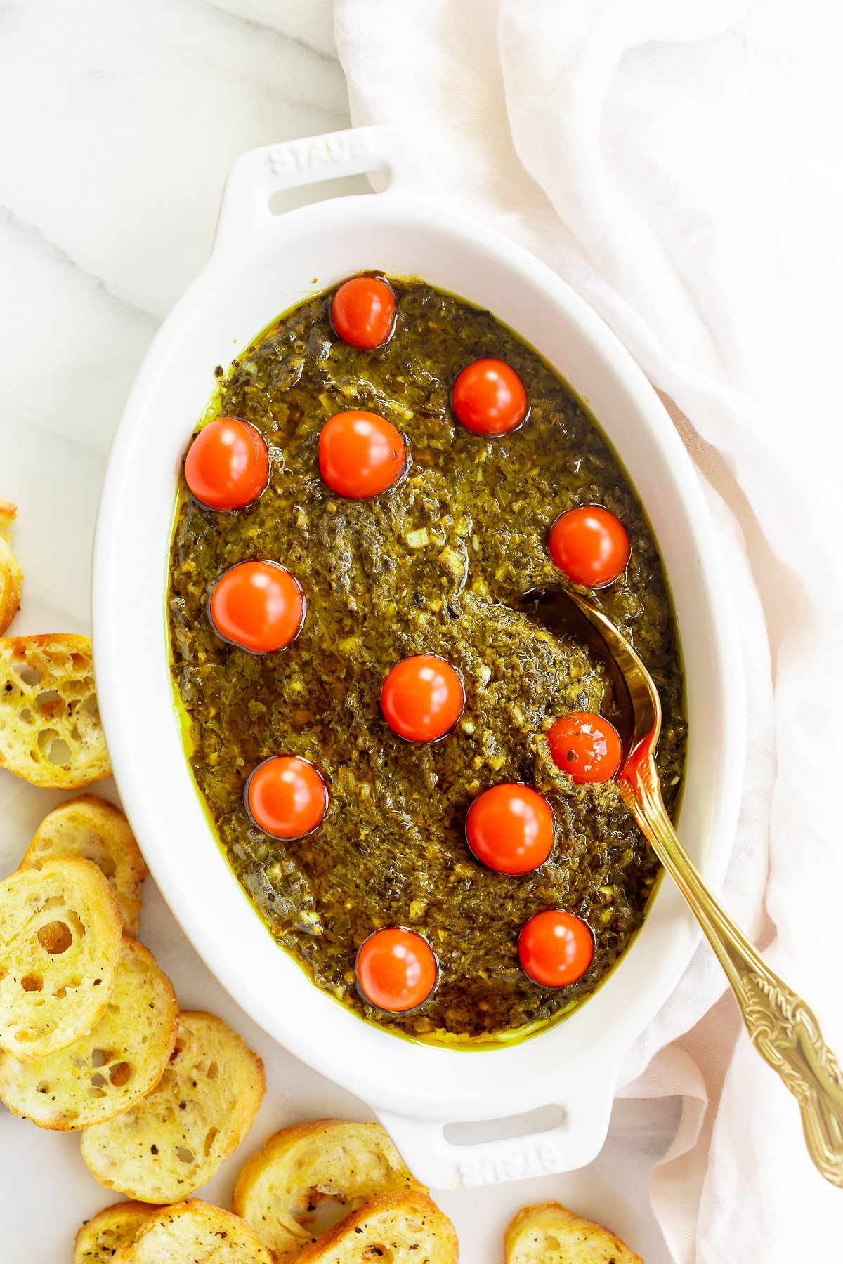 An easy appetizer dip; a white bowl of pesto dip with tomatoes and bread.